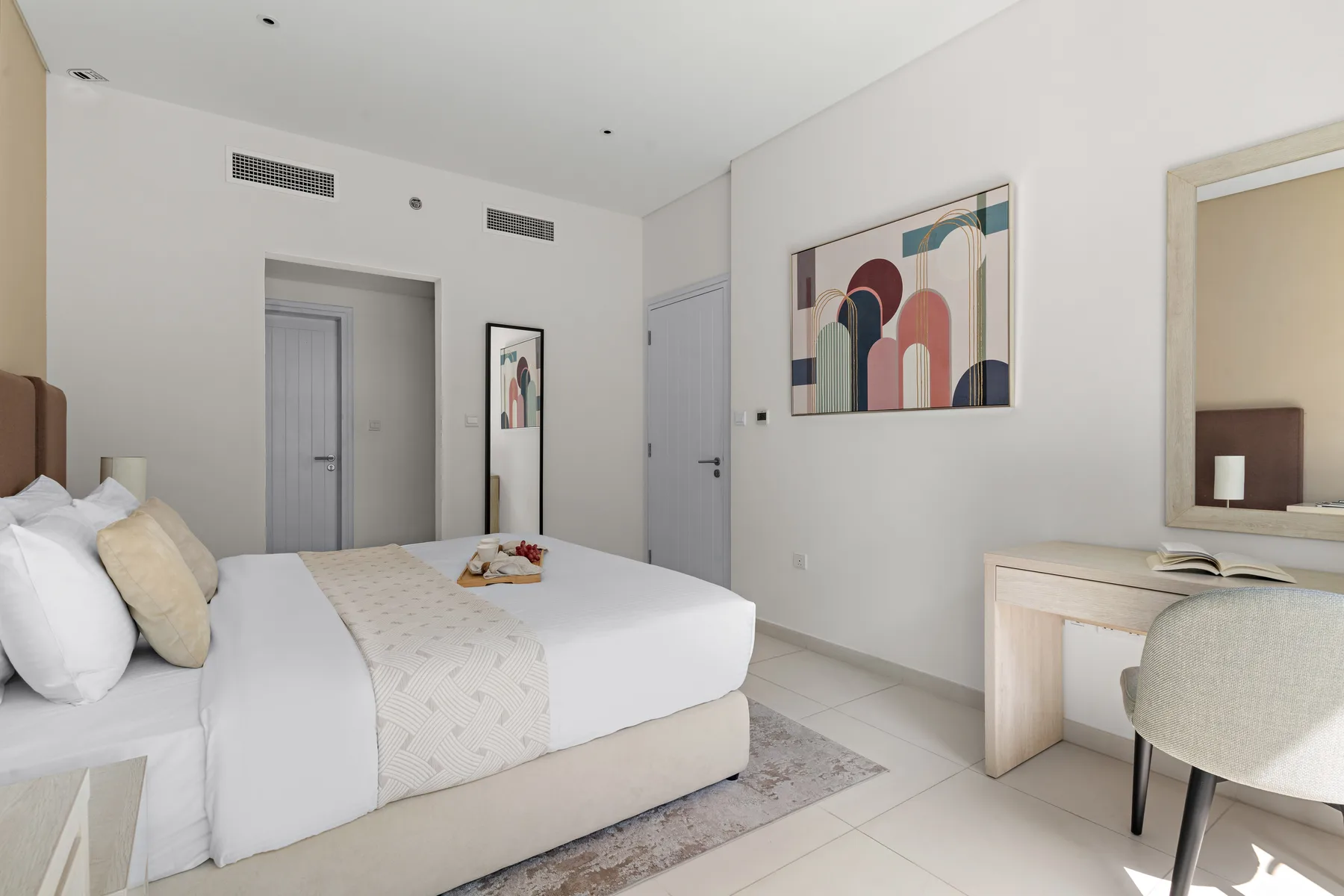 Un dormitorio luminoso con una cama bien tendida y un escritorio junto a la ventana.