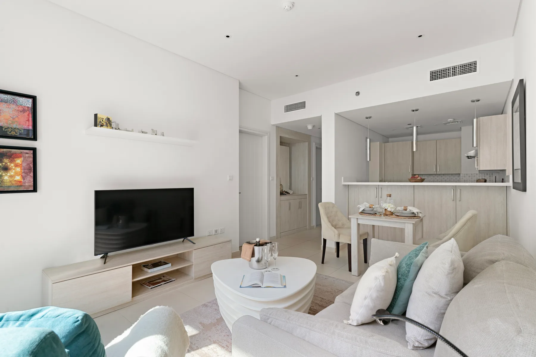Una sala luminosa con televisor, mesa de centro y cocina abierta.