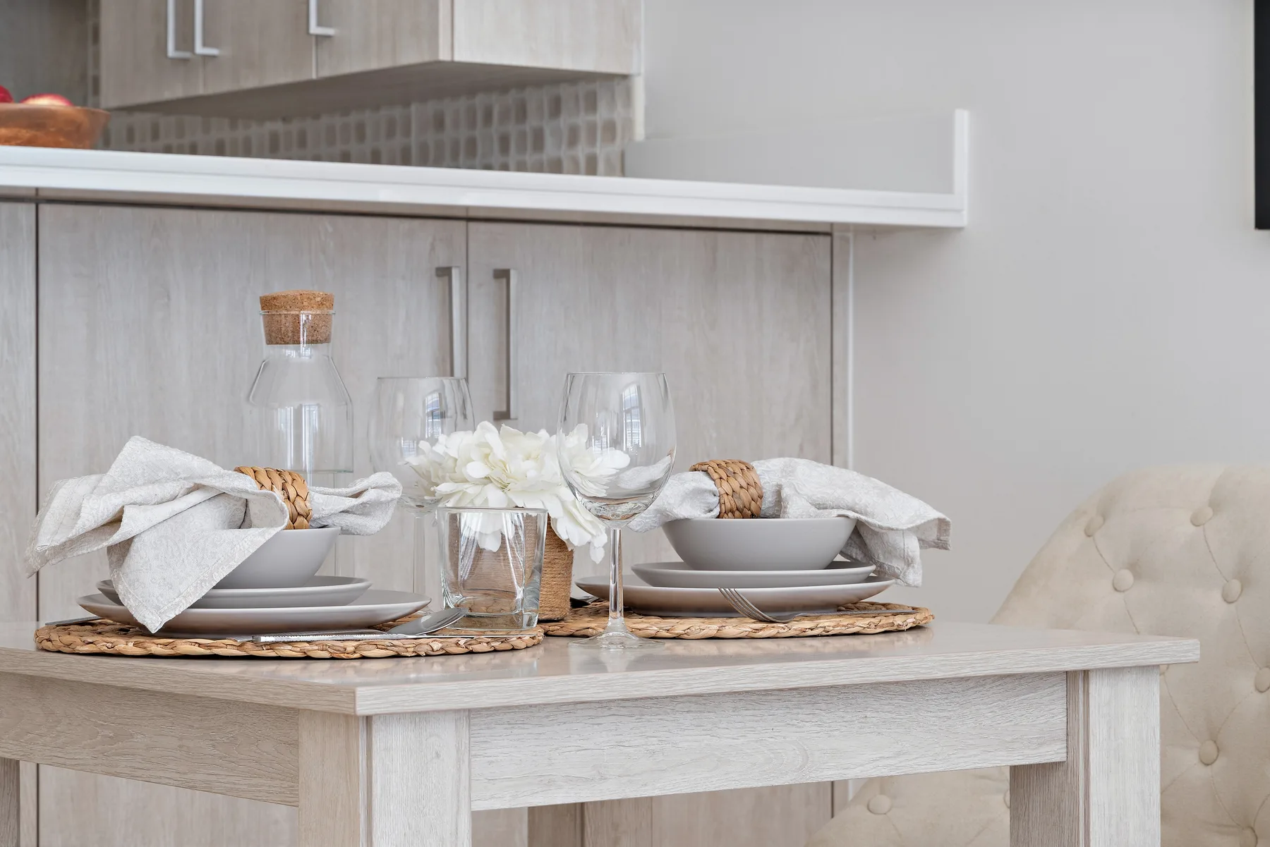 Una mesa de comedor está puesta con platos, copas, servilletas dobladas y flores.