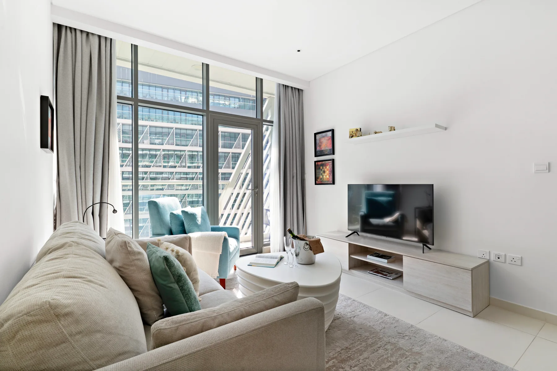 Una sala luminosa con asientos, un televisor y ventanas grandes.