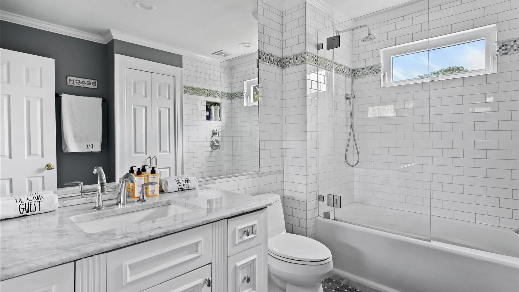 A bright bathroom features a long vanity beside a tiled bathtub and shower.