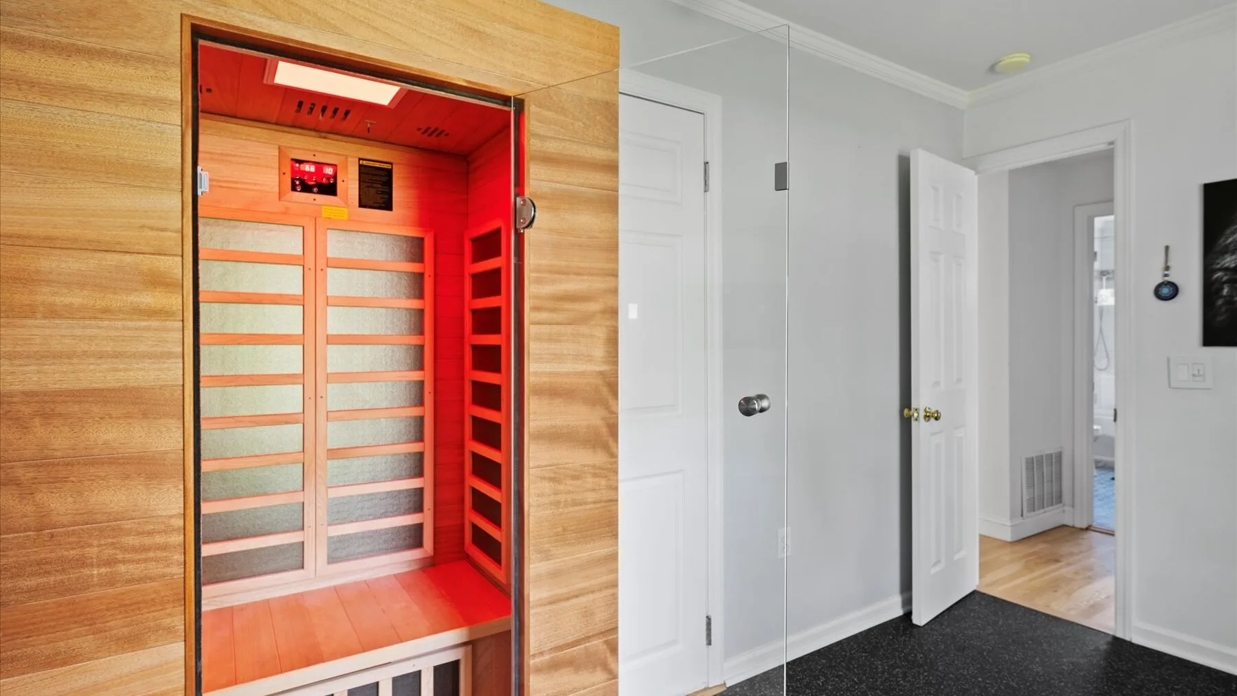 A wooden sauna cabin stands beside a white hallway with open doors.