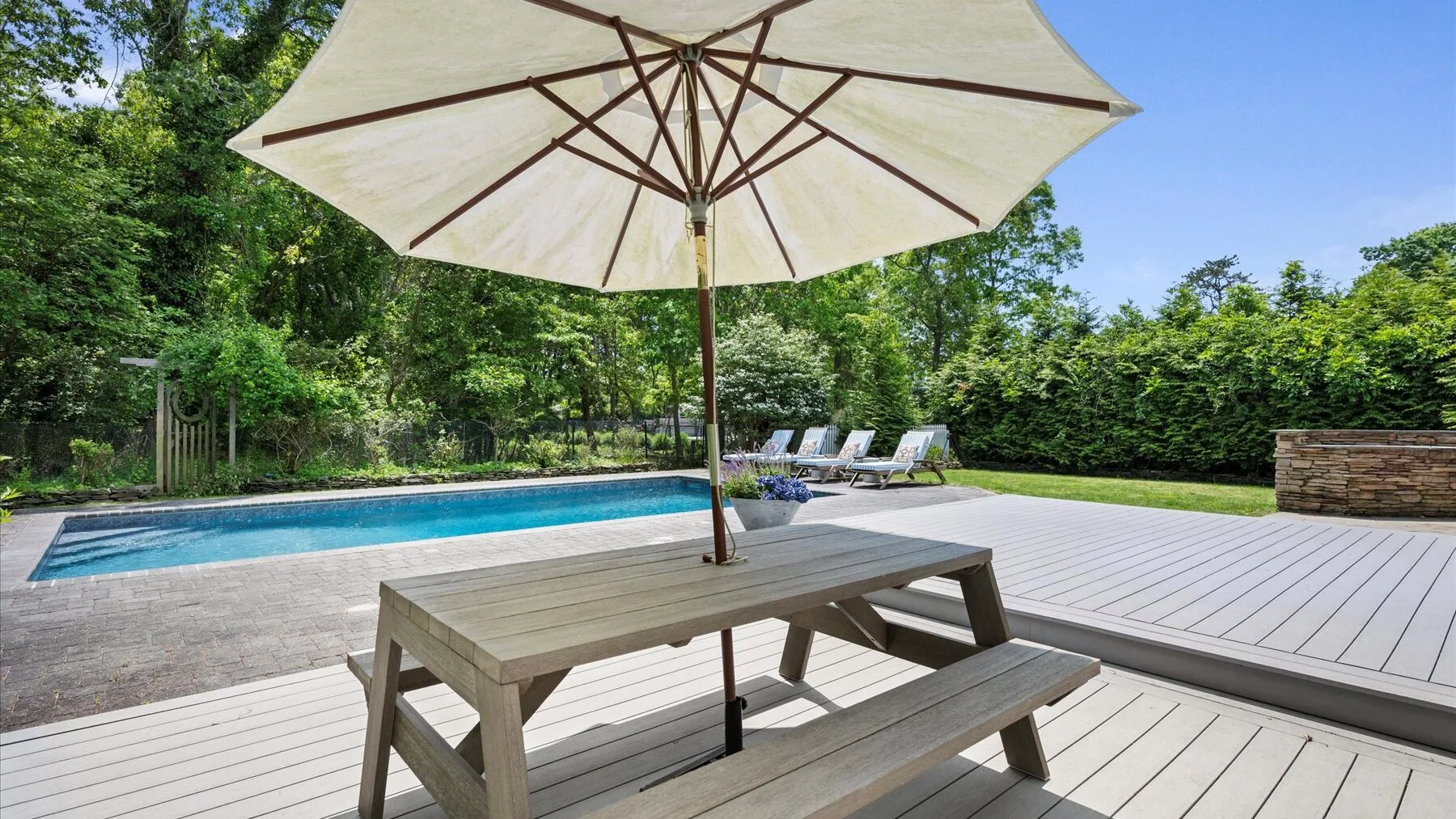 A poolside deck features a picnic table beneath a large umbrella.