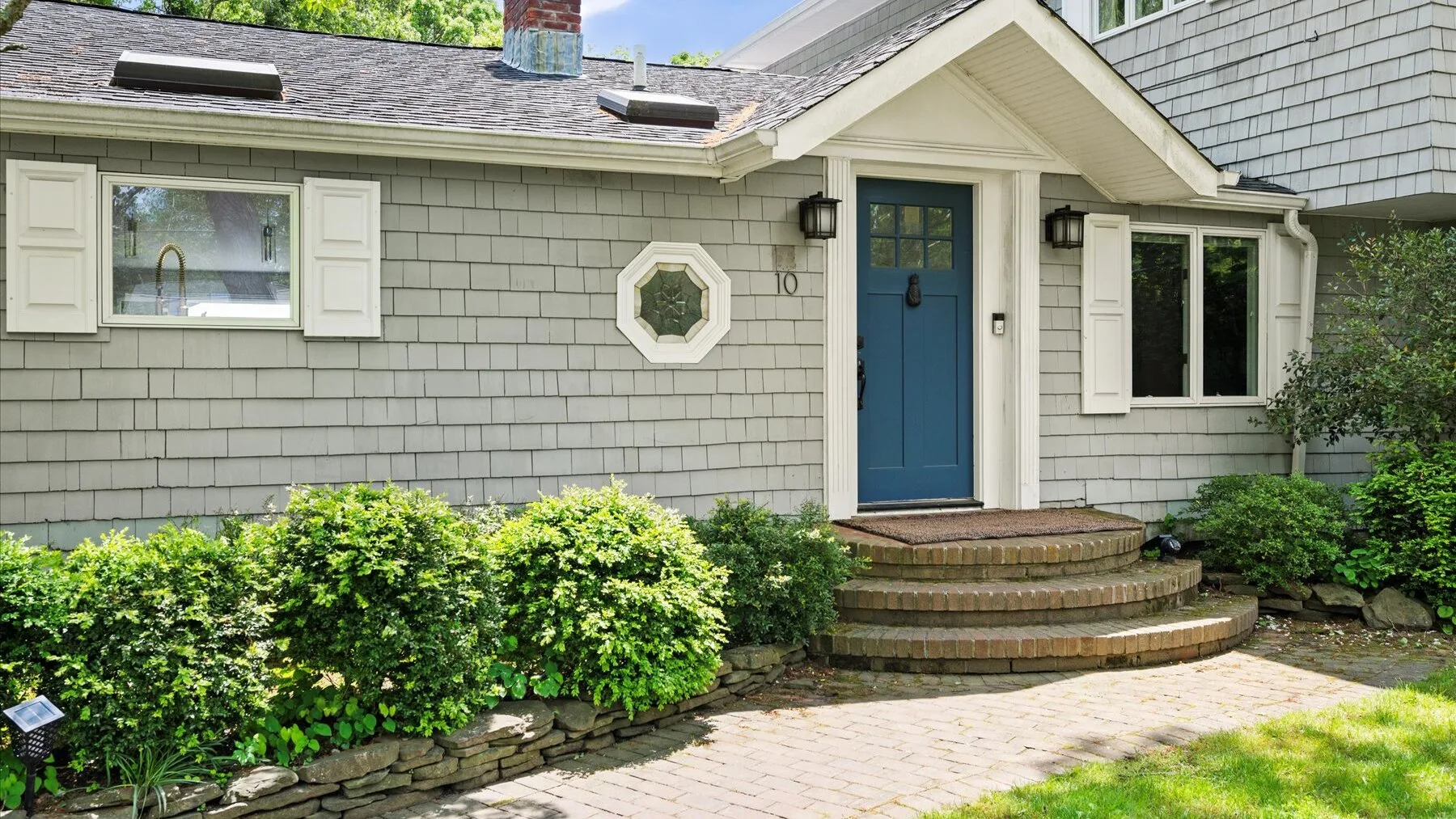 A cottage exterior with a blue front door, brick steps, and shrubs along the walkway.
