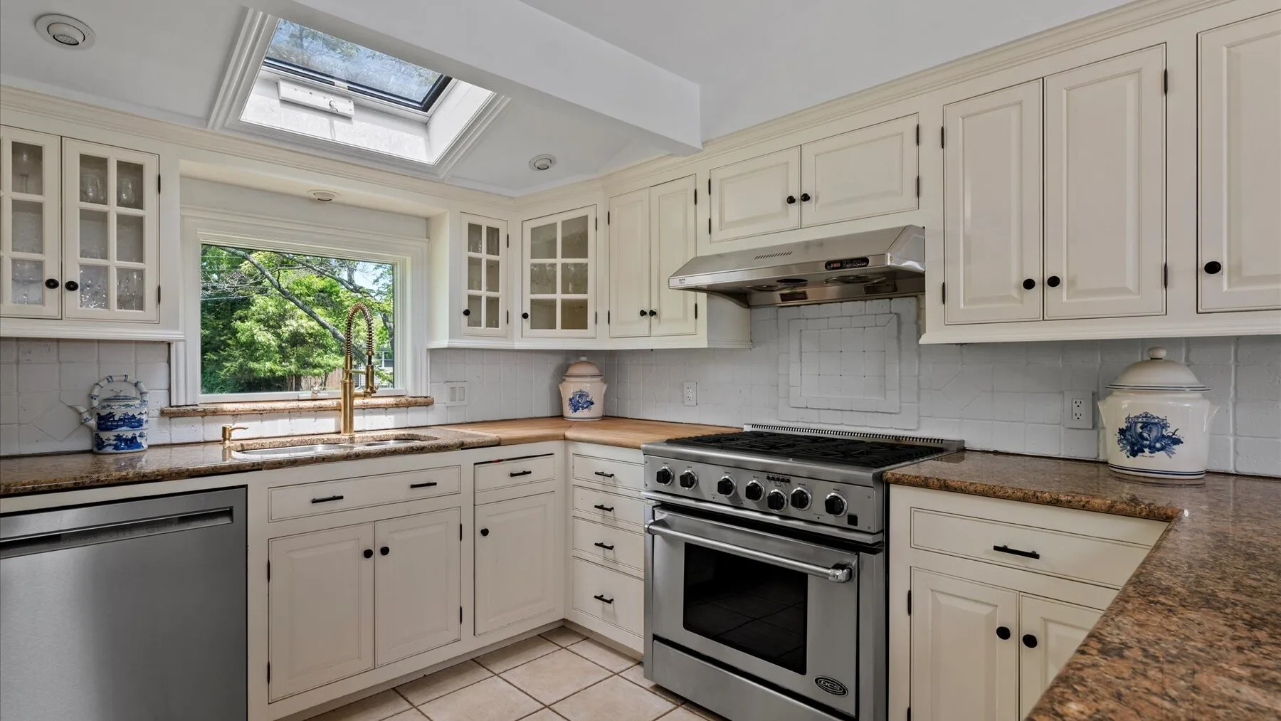 A bright kitchen with white cabinets, a stainless-steel range, and a skylight.