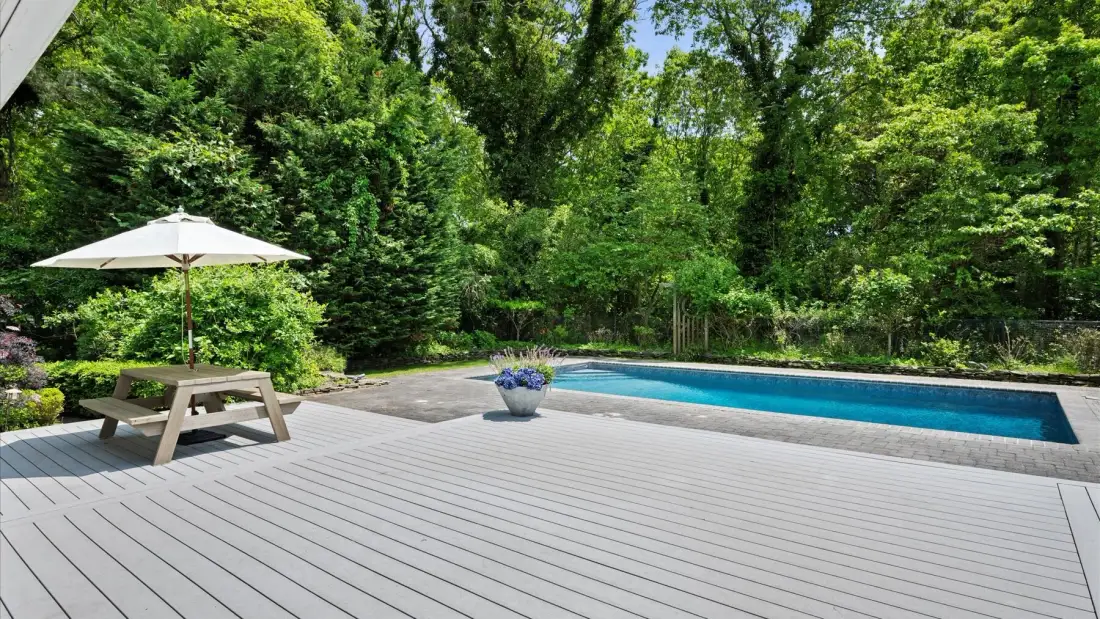 An outdoor pool sits beside a spacious deck surrounded by trees.