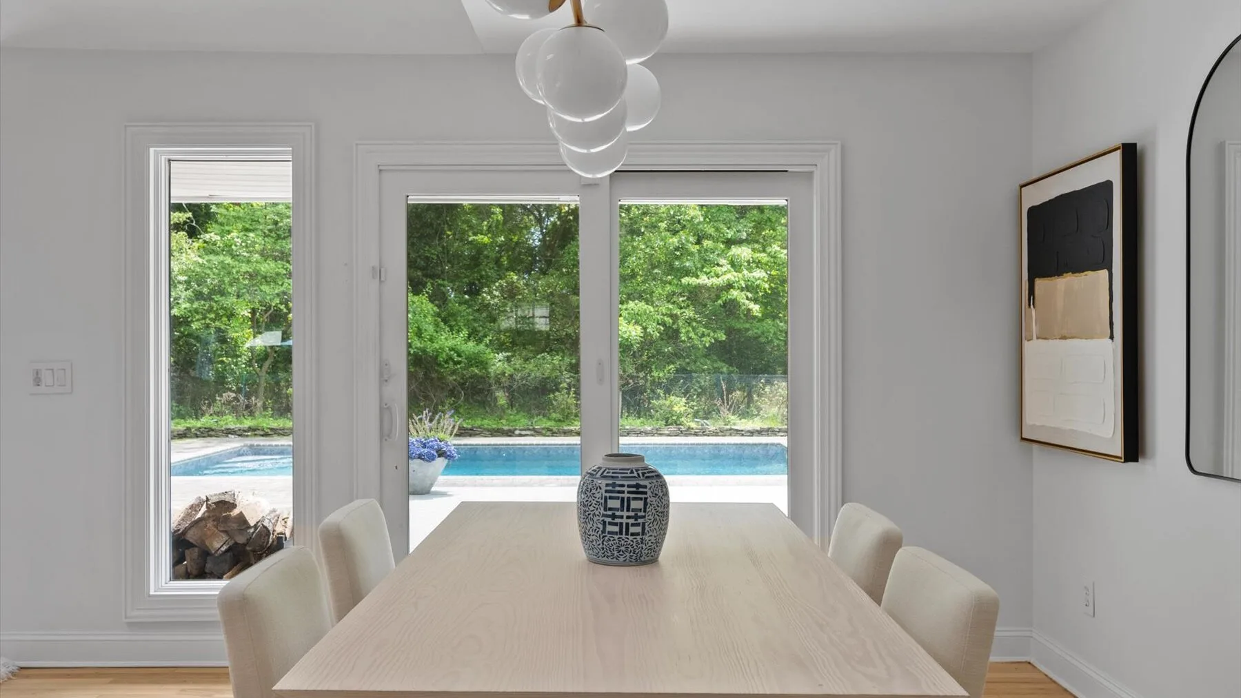A bright dining room with a long table and large windows overlooking greenery.
