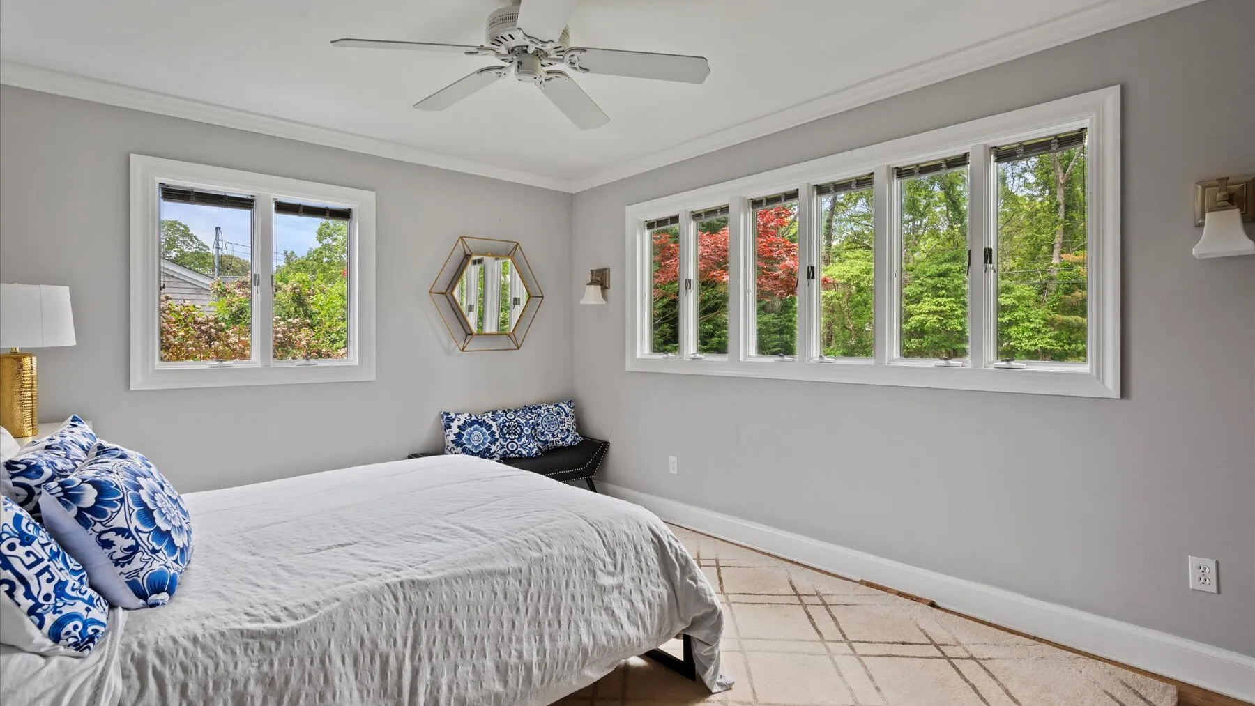 A bedroom with a bed and wide windows overlooking green trees.