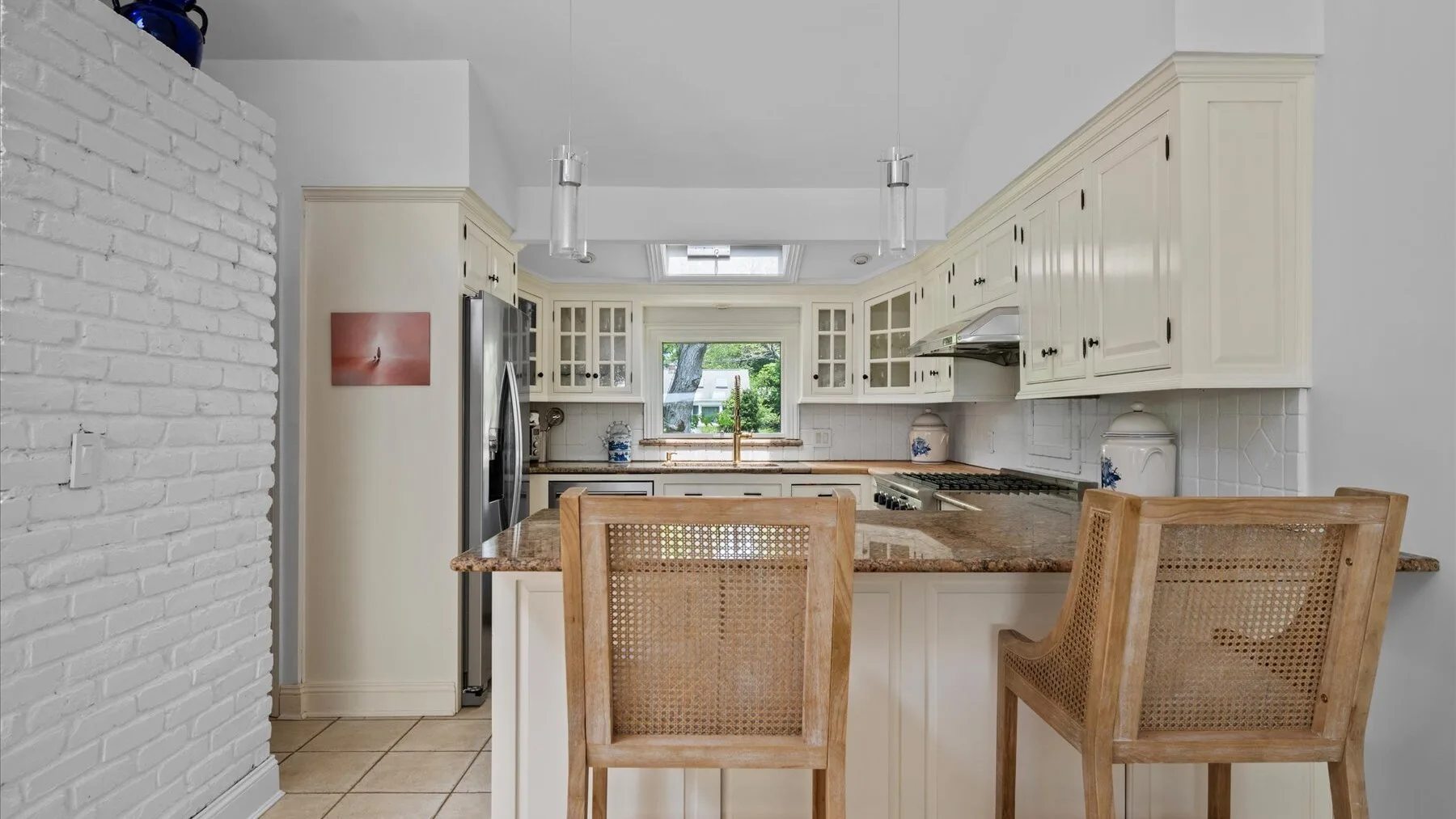 A bright kitchen with a central island, cabinetry, and woven seating.