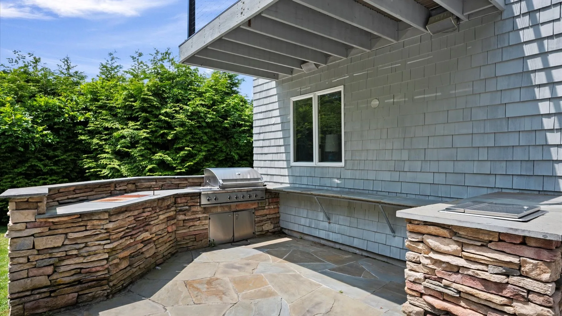An outdoor patio with stone paving, a built-in grill, and a window.