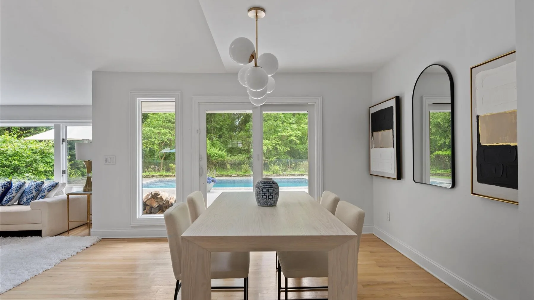A bright dining area with a long table beside large windows overlooking greenery.