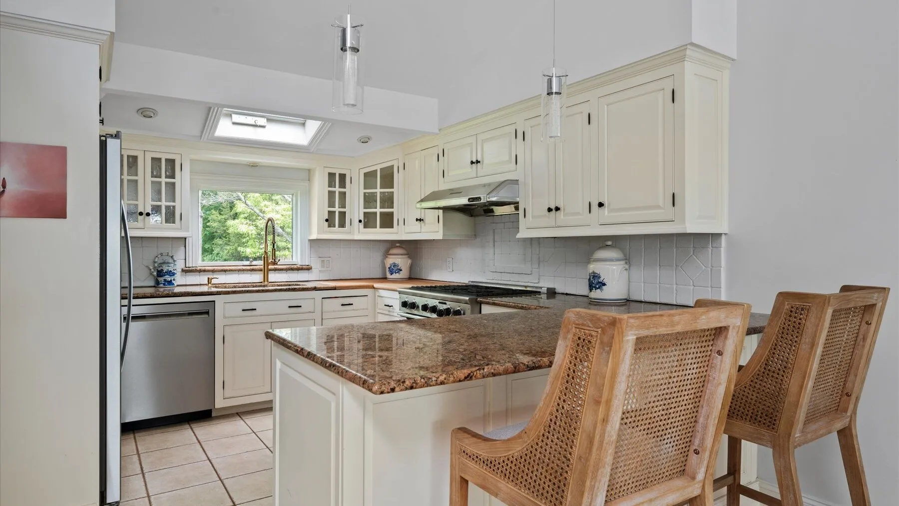 A bright kitchen with a central island, stone countertop, and woven-back seating.
