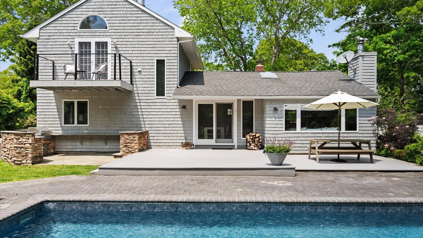 A house with a deck and outdoor seating overlooks a swimming pool.