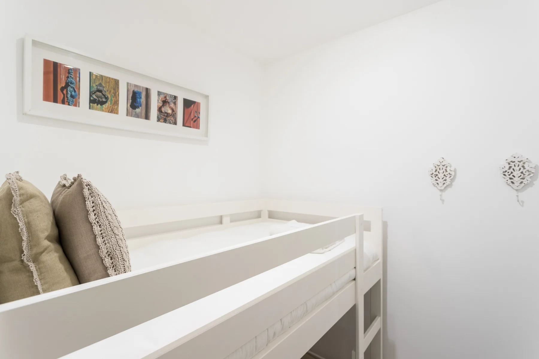 A bright bedroom with a white bunk bed and framed artwork on the wall.