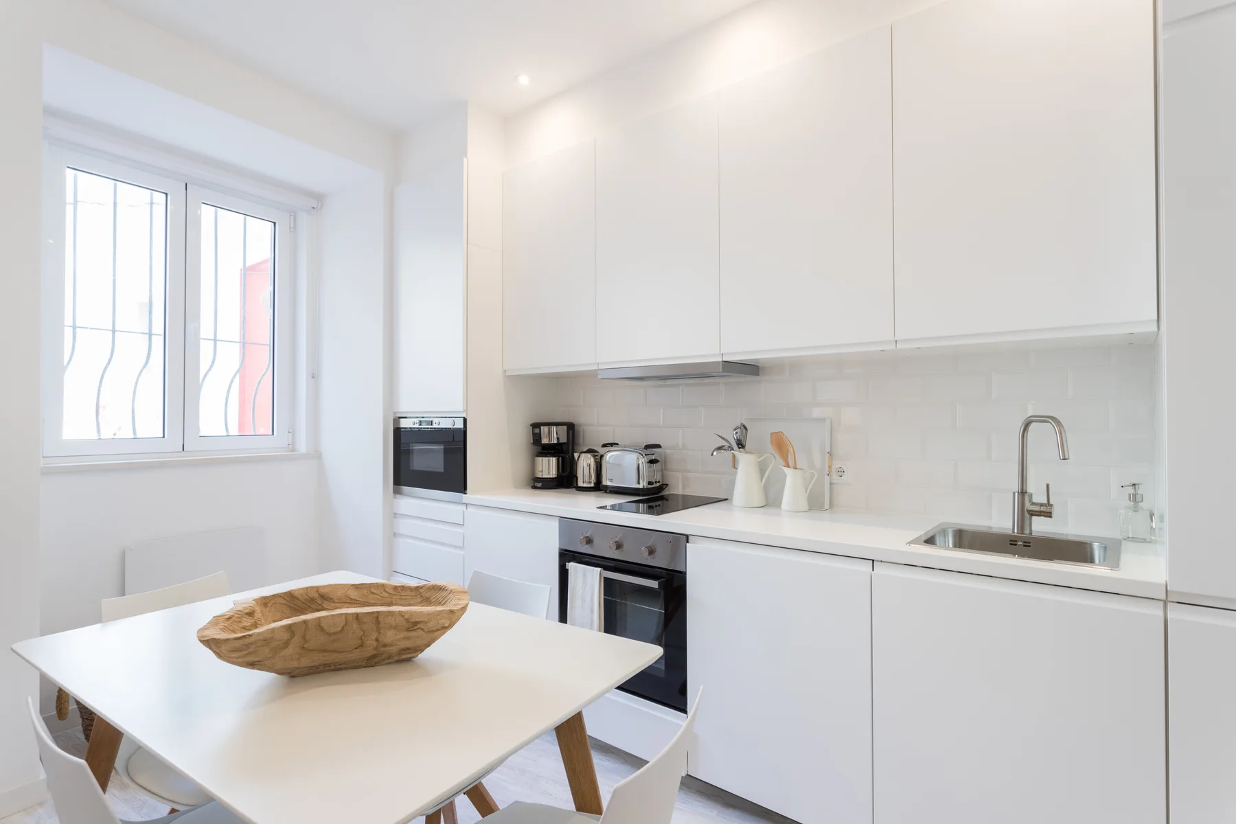 Una cocina luminosa con comedor, muebles blancos, una mesa y una ventana.