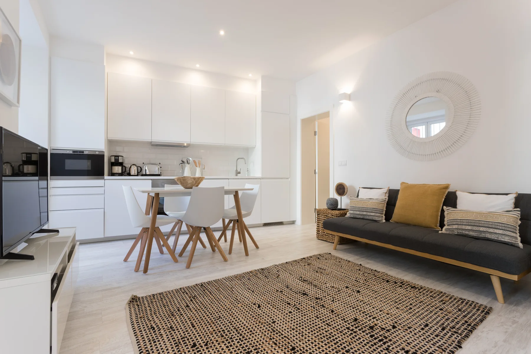A bright living and dining area with a dark sofa and a table beside the kitchen.