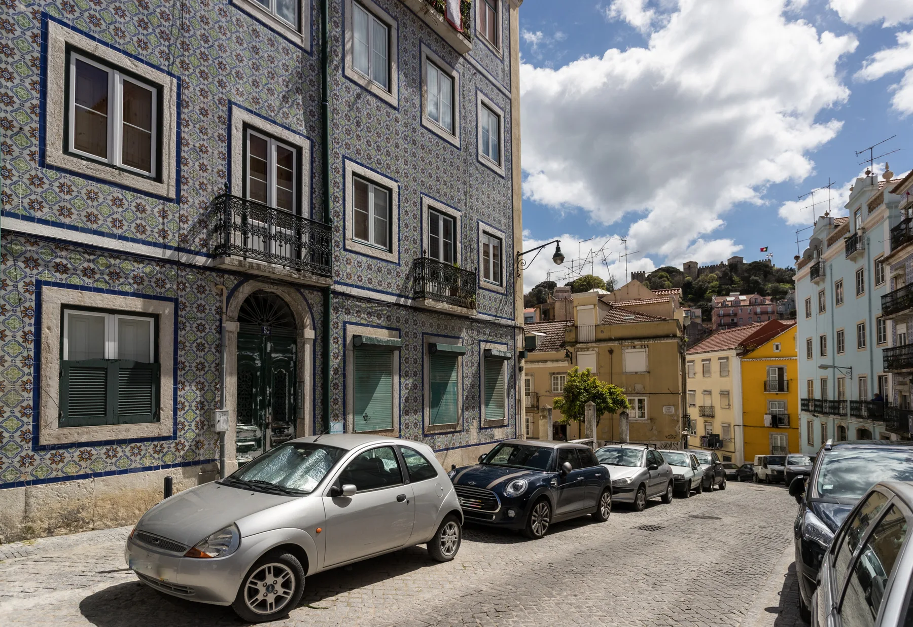A city street lined with parked cars and buildings decorated with patterned tiles.