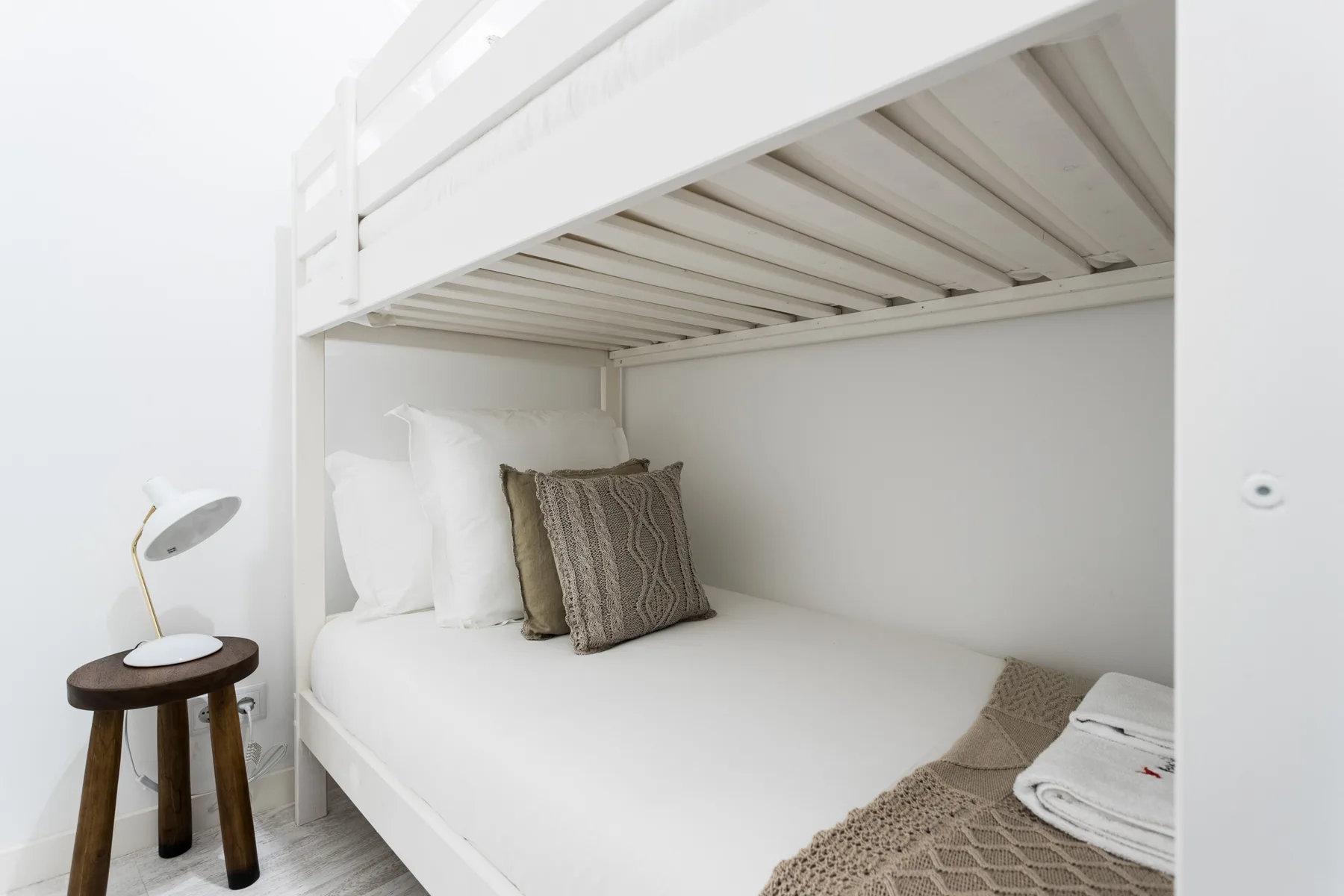 A white bed sits beneath an elevated bunk in a bright bedroom.
