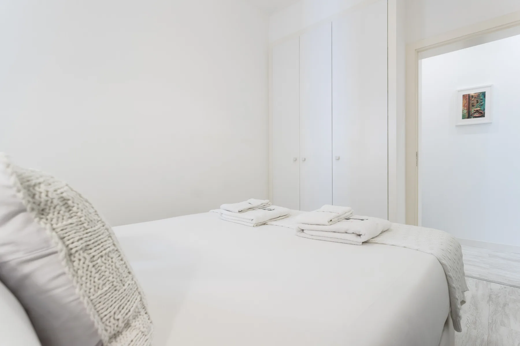 A bright bedroom with a neatly made bed and folded towels.