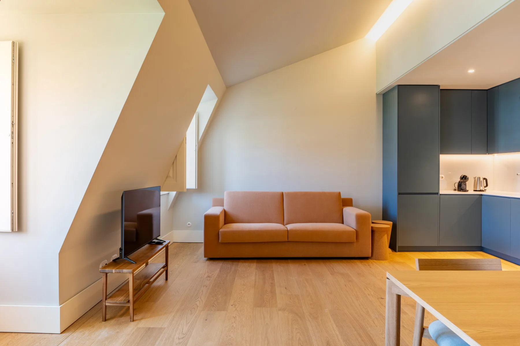 Una sala de estar con asientos naranjas, un televisor y una cocina contigua.