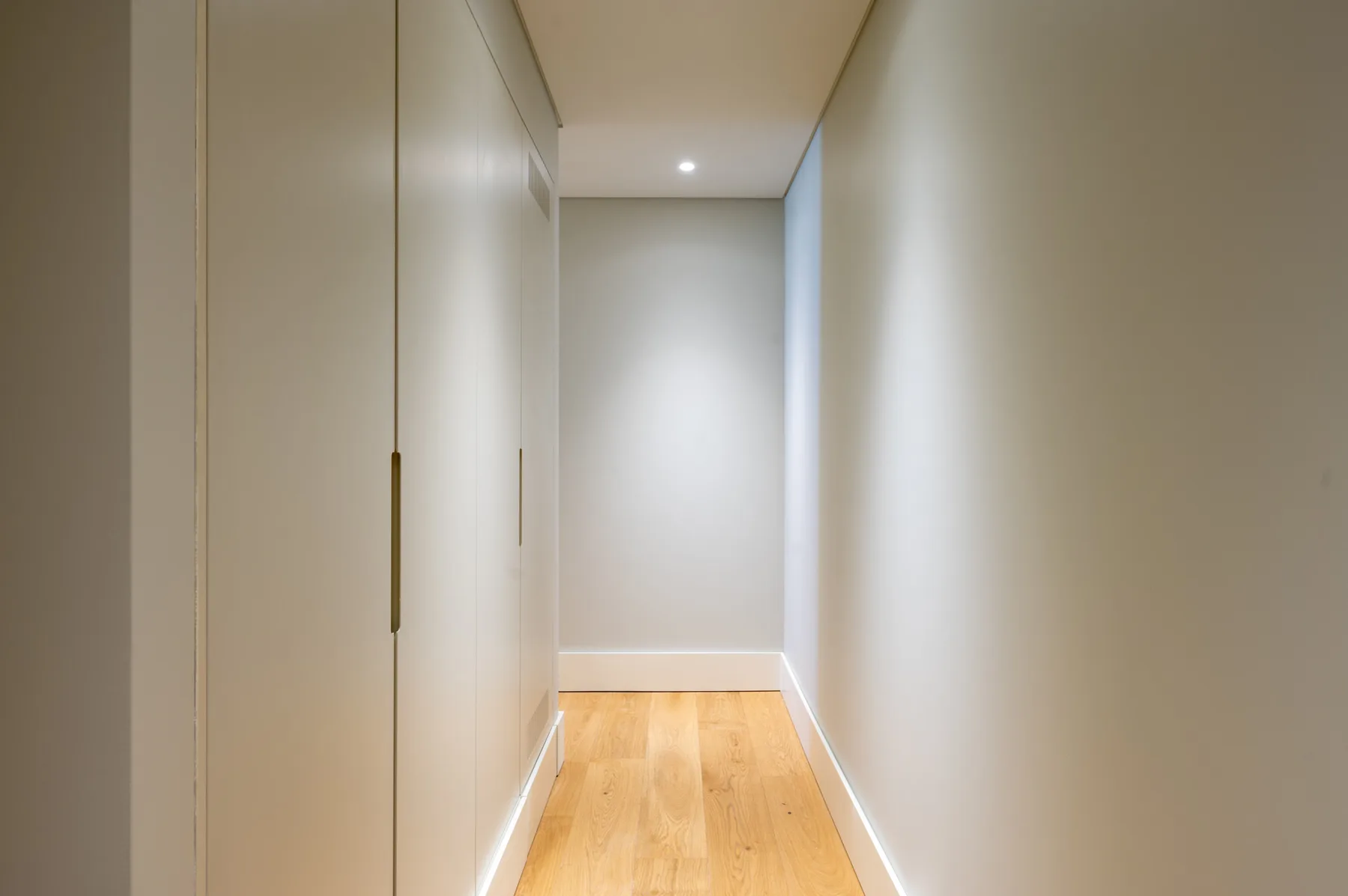 Un pasillo estrecho con suelo de madera clara y armarios empotrados.