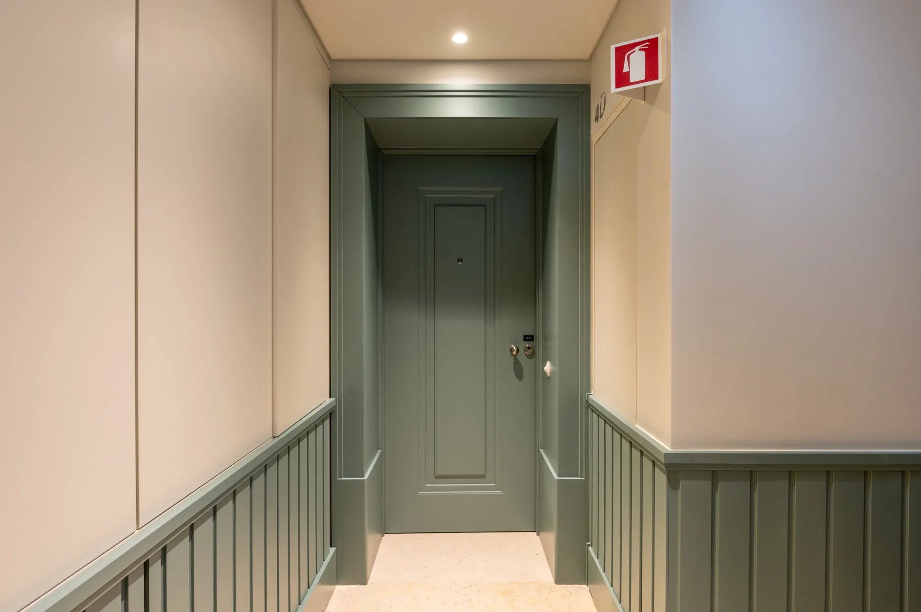 Un pasillo con paredes paneladas conduce a una puerta cerrada.