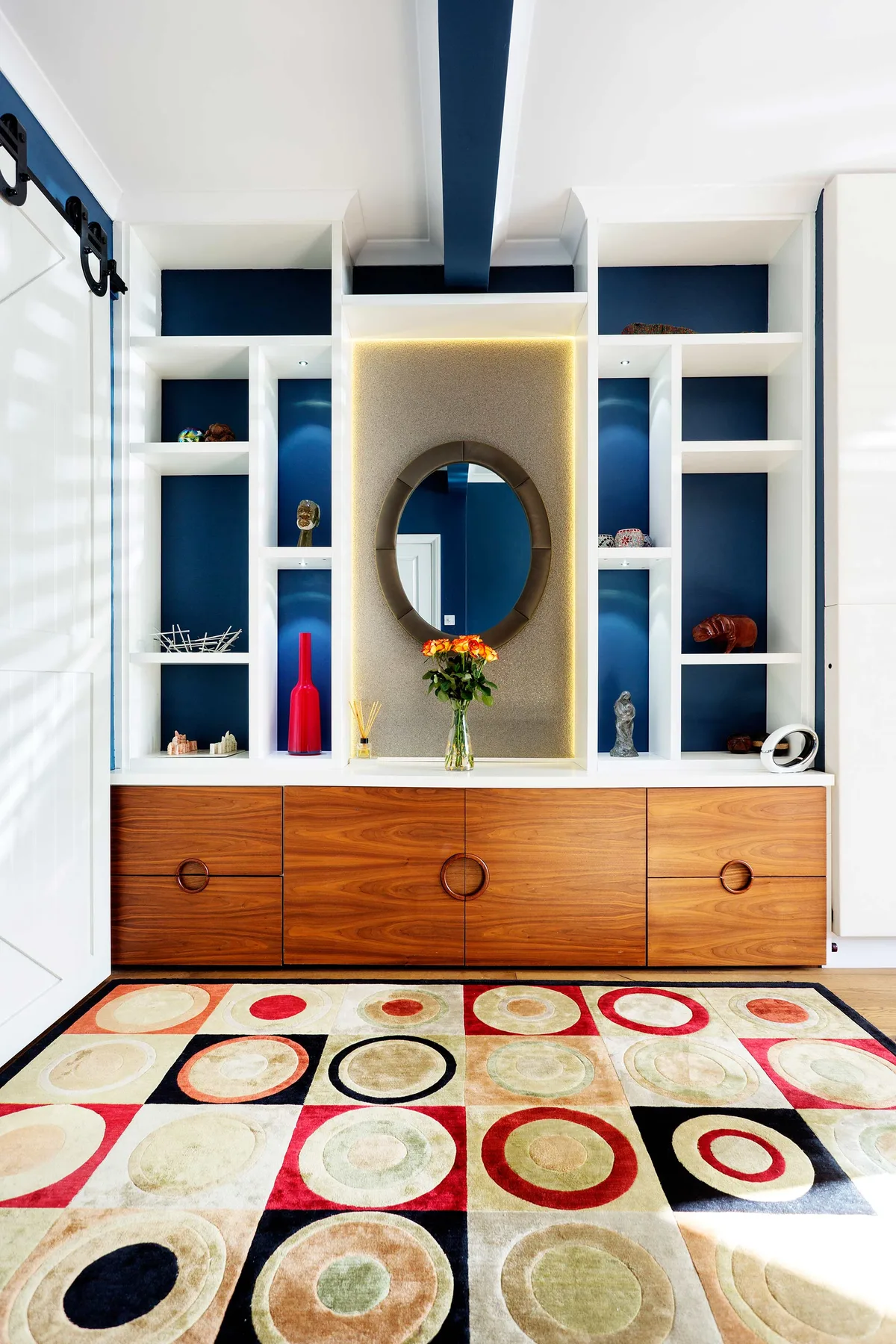 A white built-in display cabinet with a round mirror above wooden drawers.