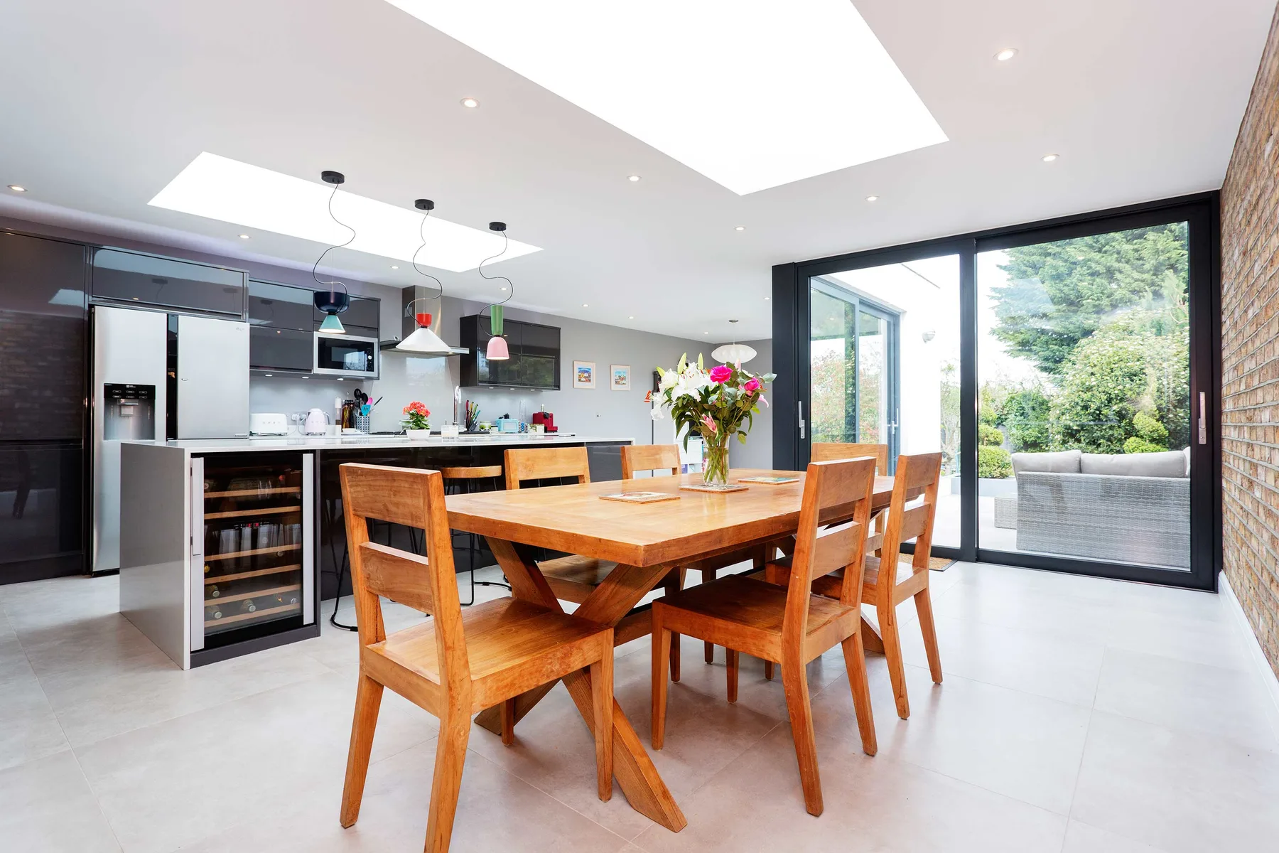 A bright dining area with a wooden table beside an open kitchen and large glass doors.