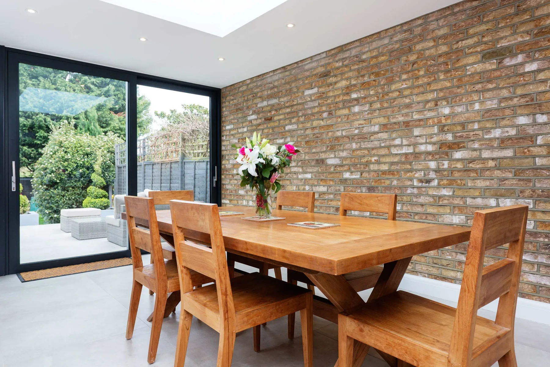 A dining area with a wooden table and chairs beside large glass doors.