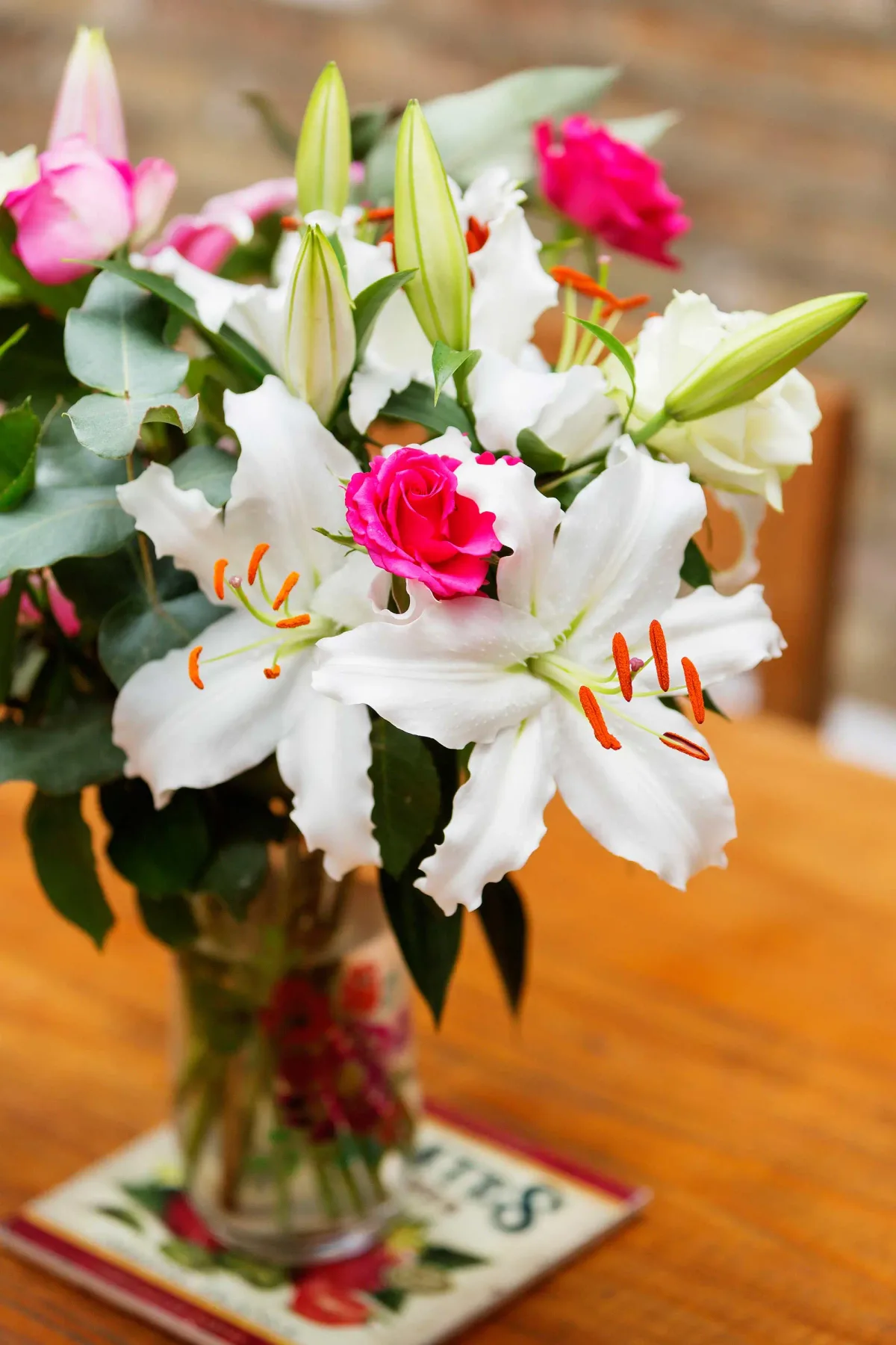 A floral arrangement of white lilies and pink roses sits in a glass vase.