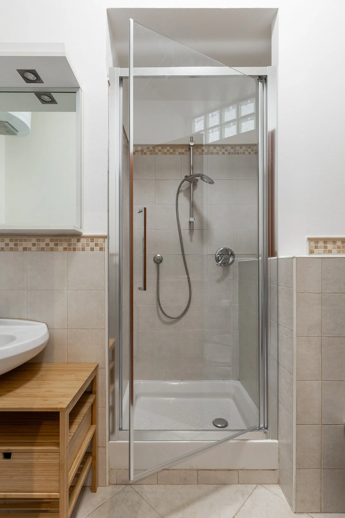 A bathroom shower with a handheld showerhead and tiled walls.