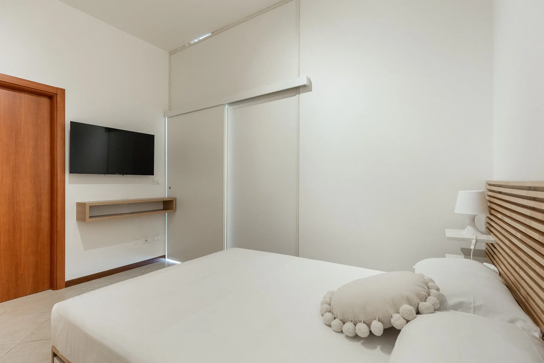 A bright bedroom with a bed, wall-mounted television, and wooden headboard.