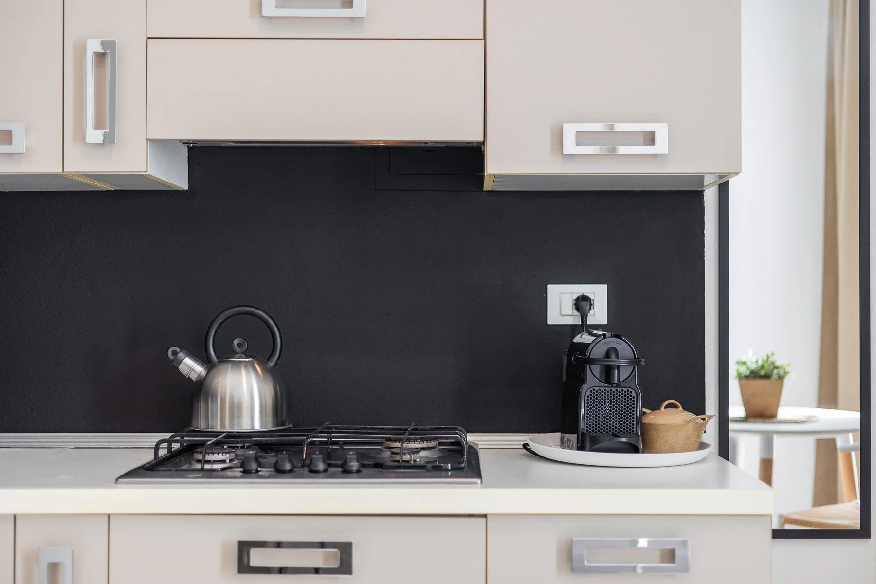 A kitchen counter with a stovetop, kettle, and coffee maker against a dark backsplash.