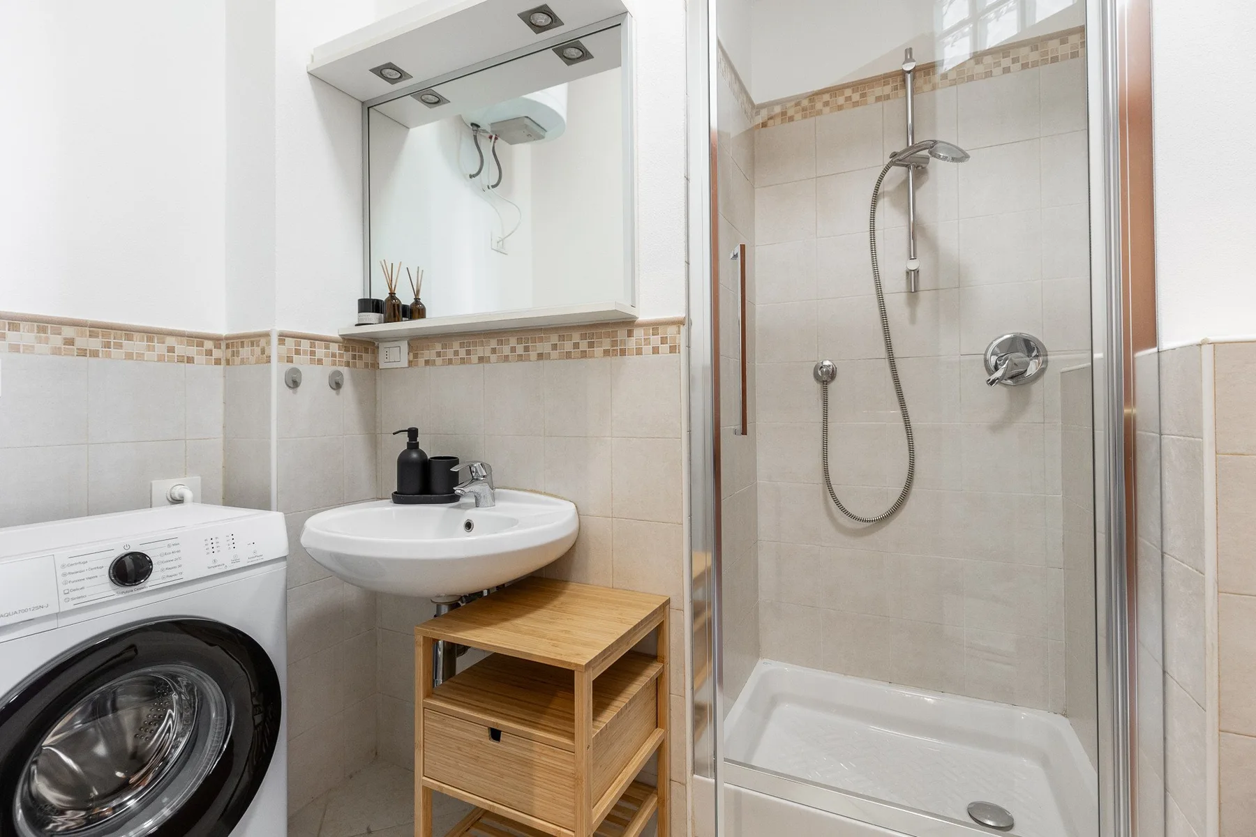 A bathroom with a sink, washing machine, and glass-enclosed shower.