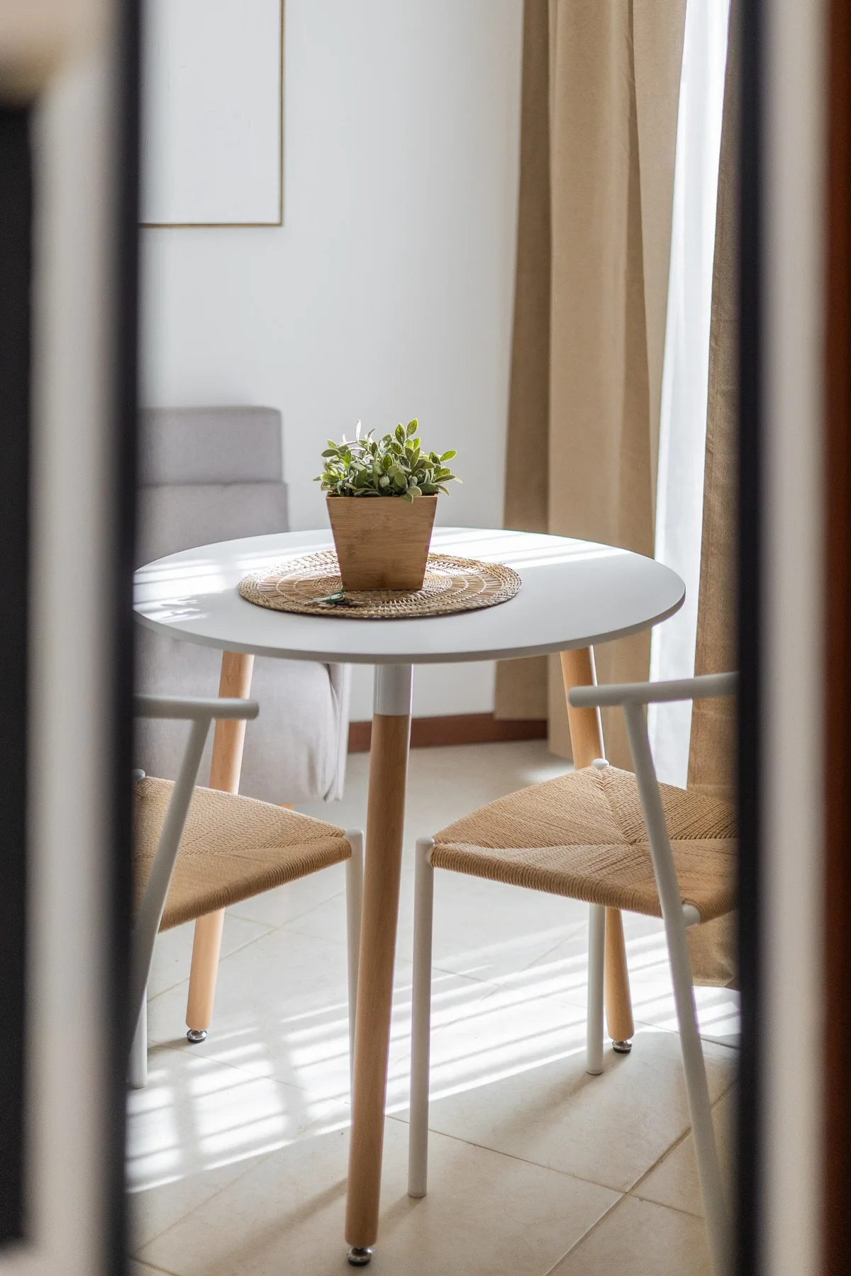 A small dining area with a round table, woven chairs, and a potted plant.