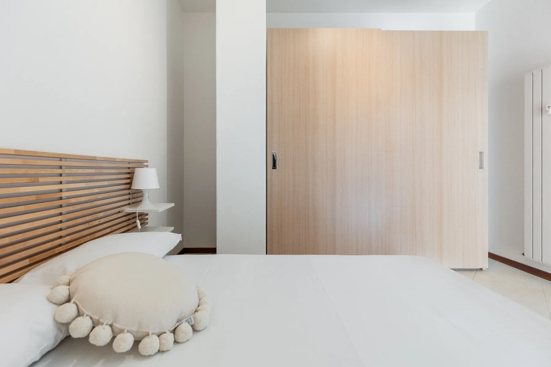 A bedroom with a bed, slatted headboard, and light wood wardrobe.
