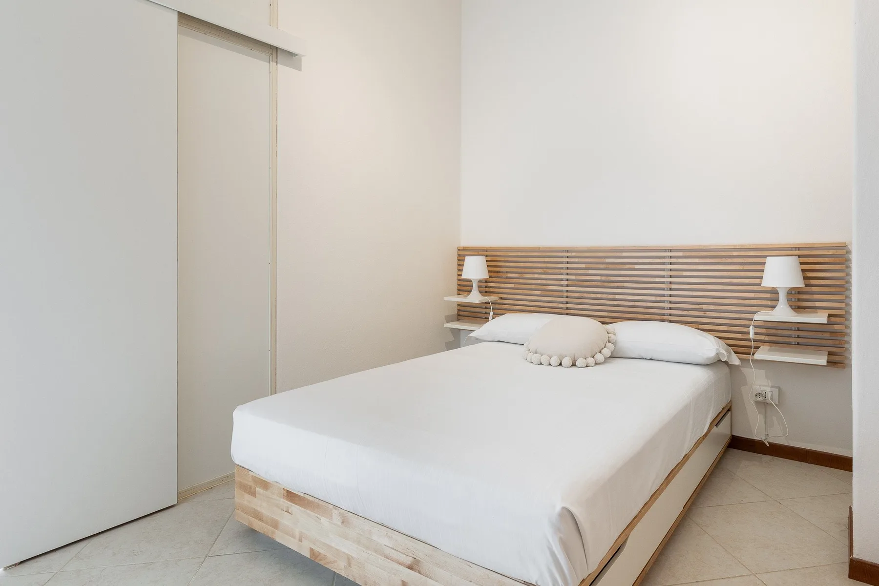 A bedroom with a neatly made bed and a wooden slatted headboard.