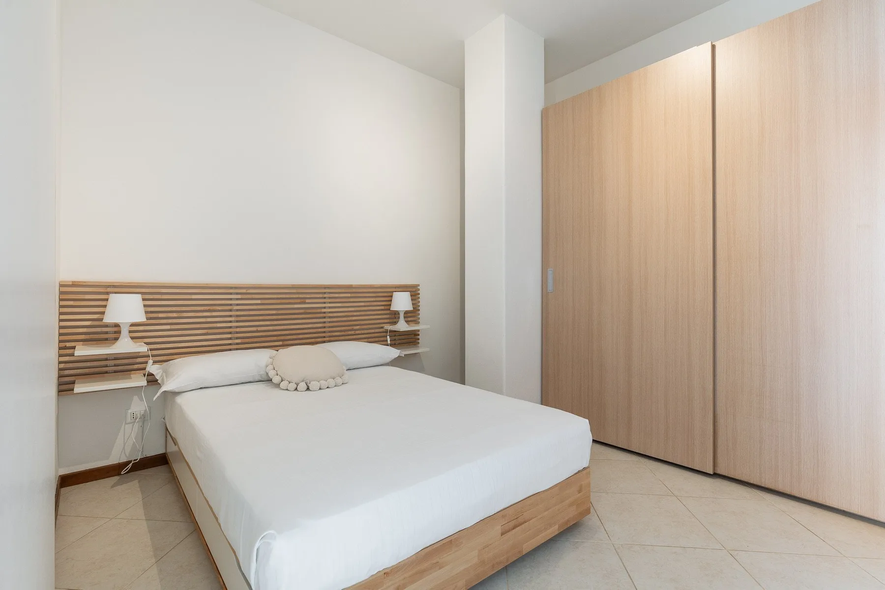A bedroom with a bed, bedside lamps, and a tall wooden wardrobe.