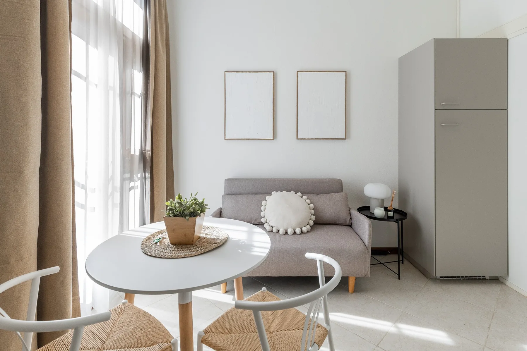 A bright living area with a sofa, round table, and tall curtained windows.