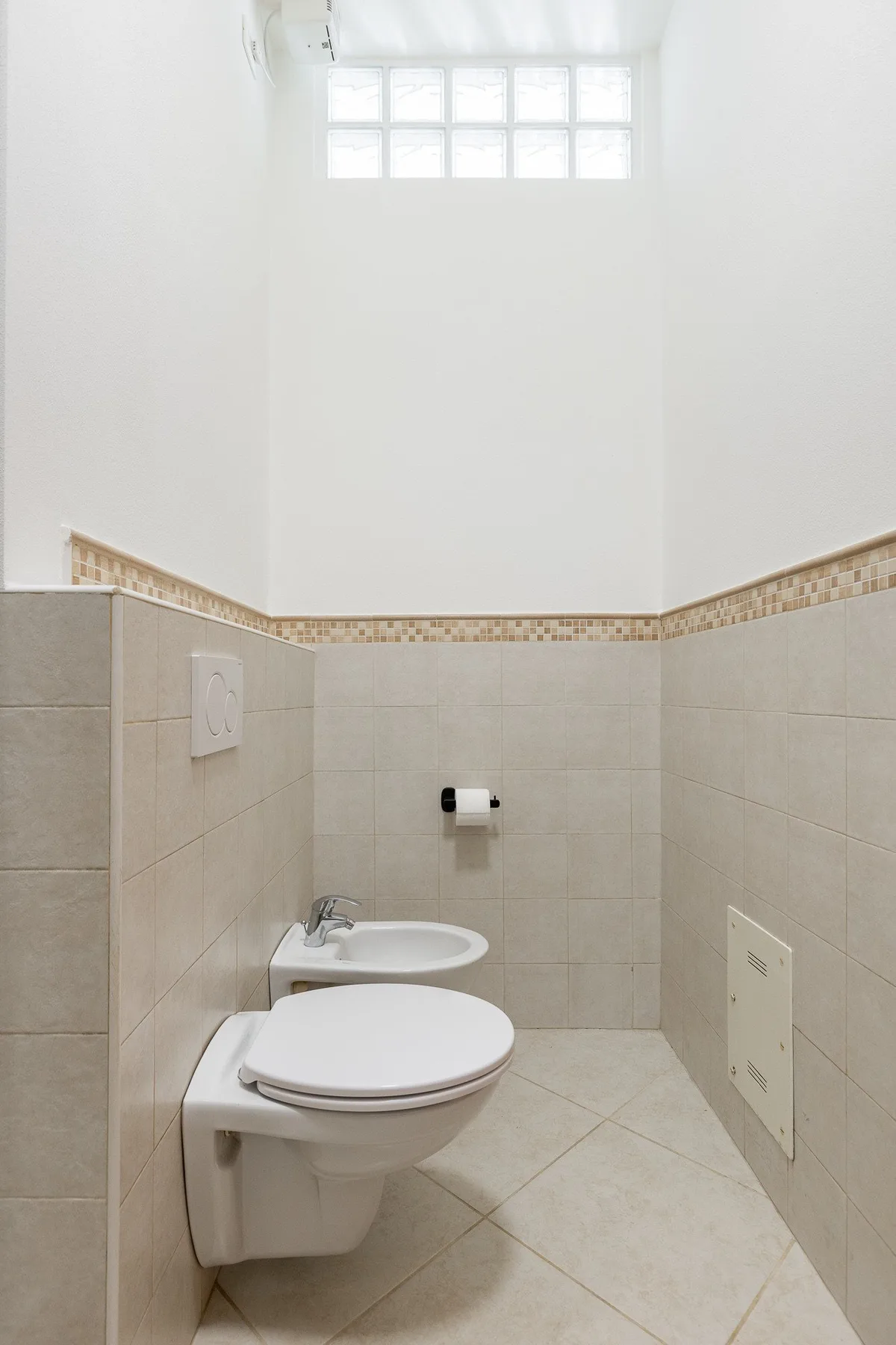 A tiled bathroom with a toilet, sink, and high window.
