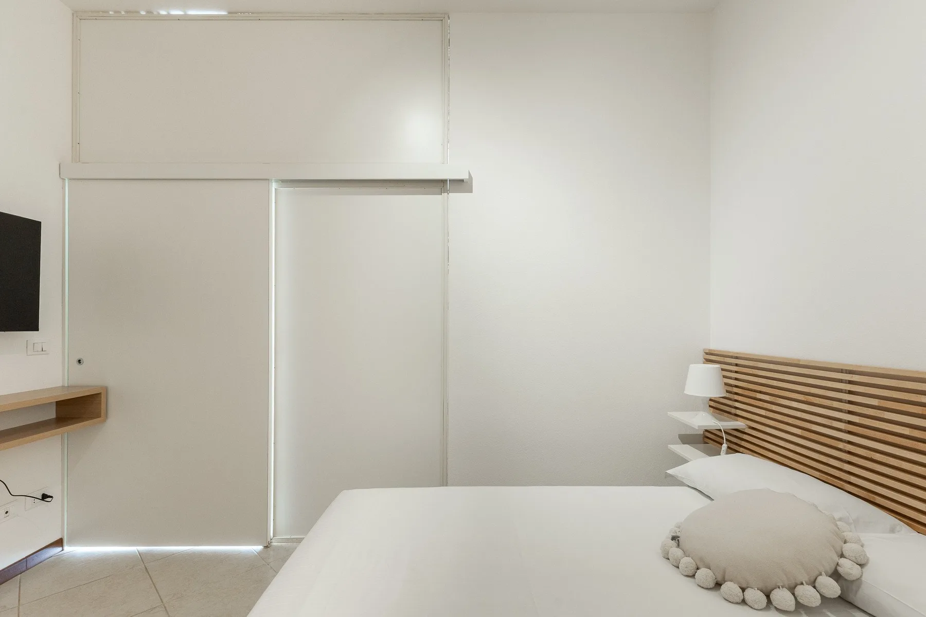 Un dormitorio con cama, cabecero de listones y televisor montado en la pared.