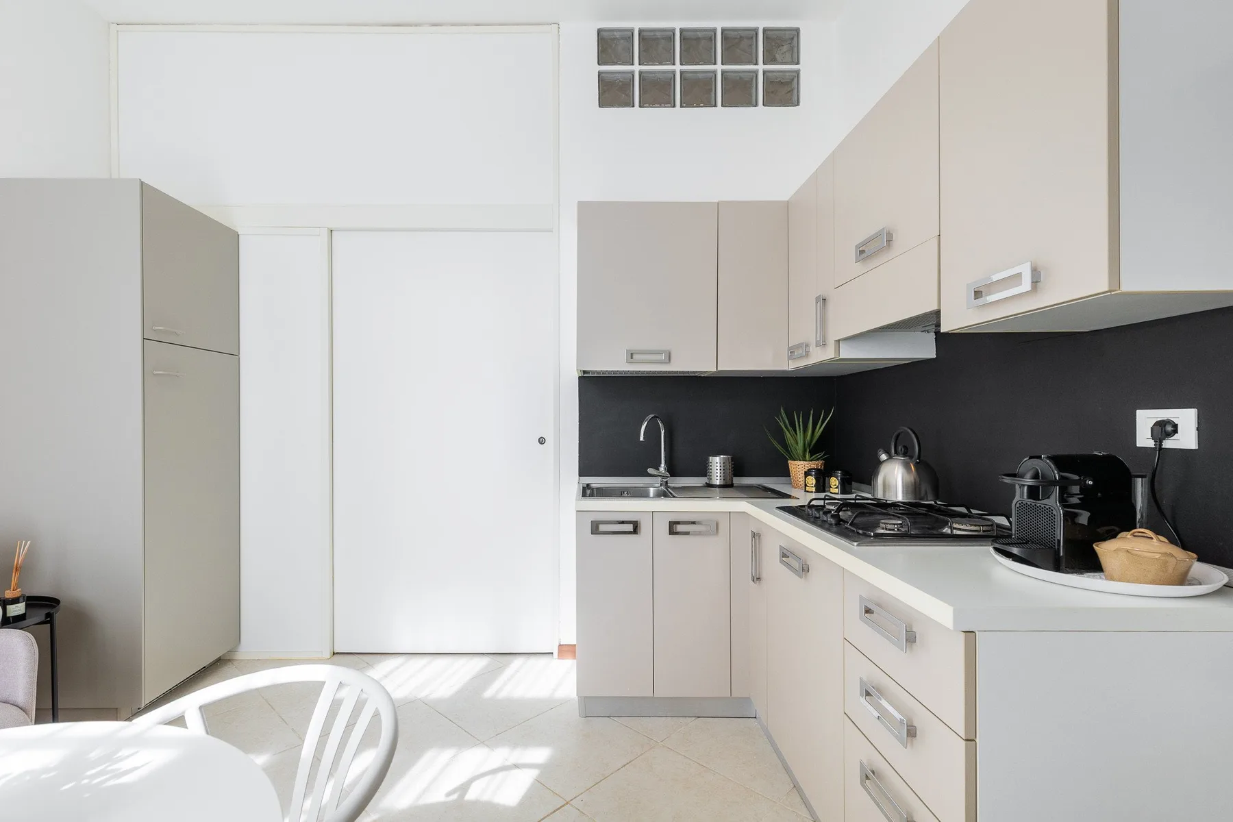 A bright kitchen with pale cabinets, a dark backsplash, and a countertop.