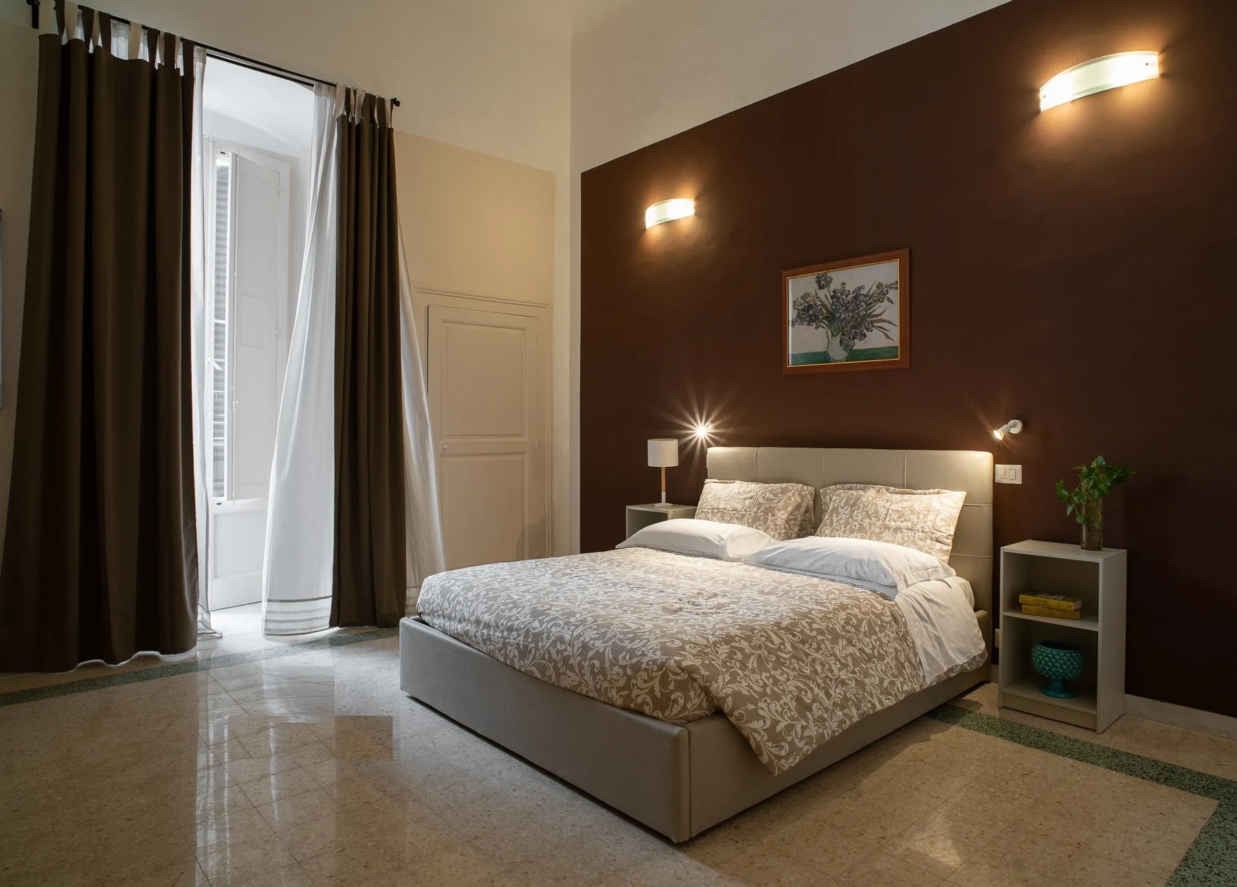 A bedroom with a neatly made bed, bedside tables, and tall curtained windows.
