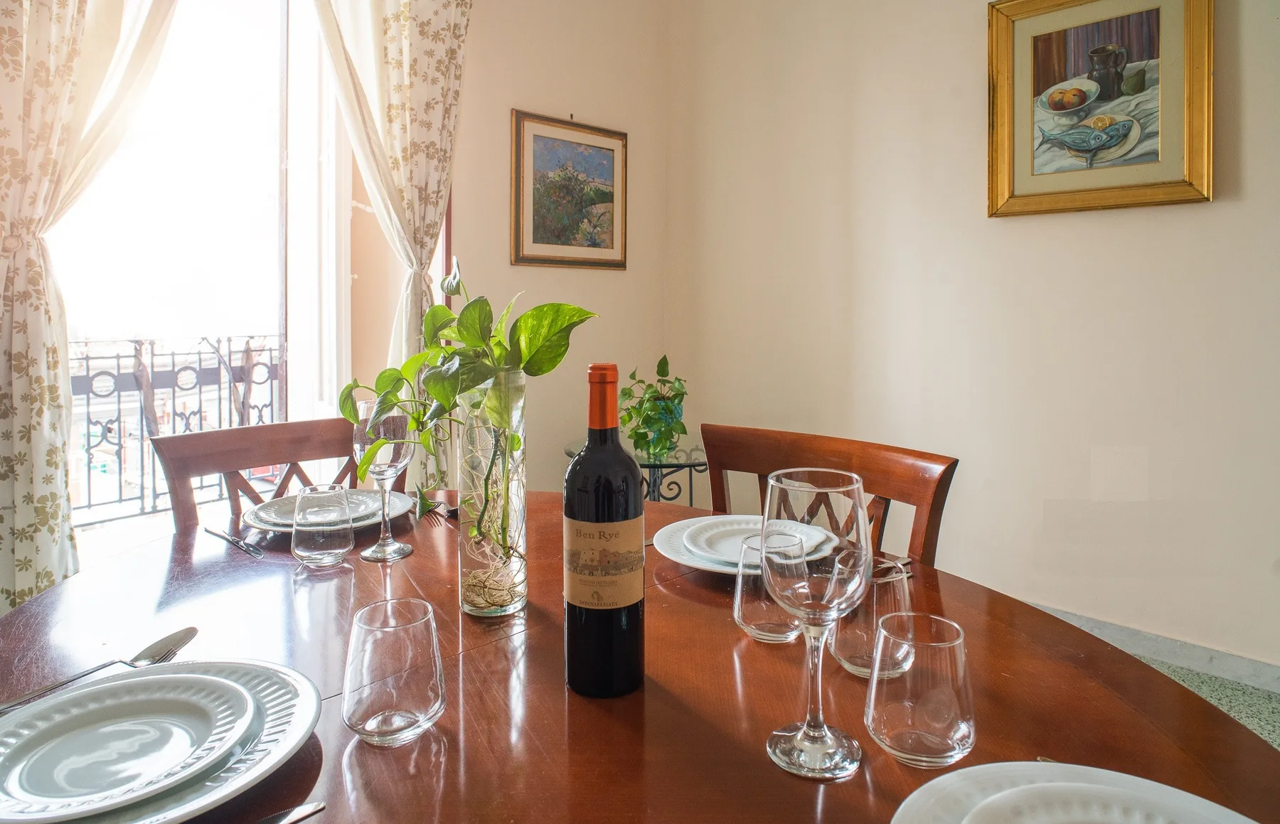 A dining table is set with plates and glasses beside a bright window.