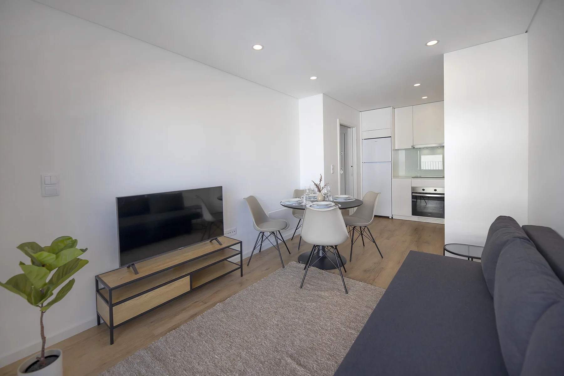 Una luminosa sala-comedor se abre a una cocina compacta, con televisor y asientos.