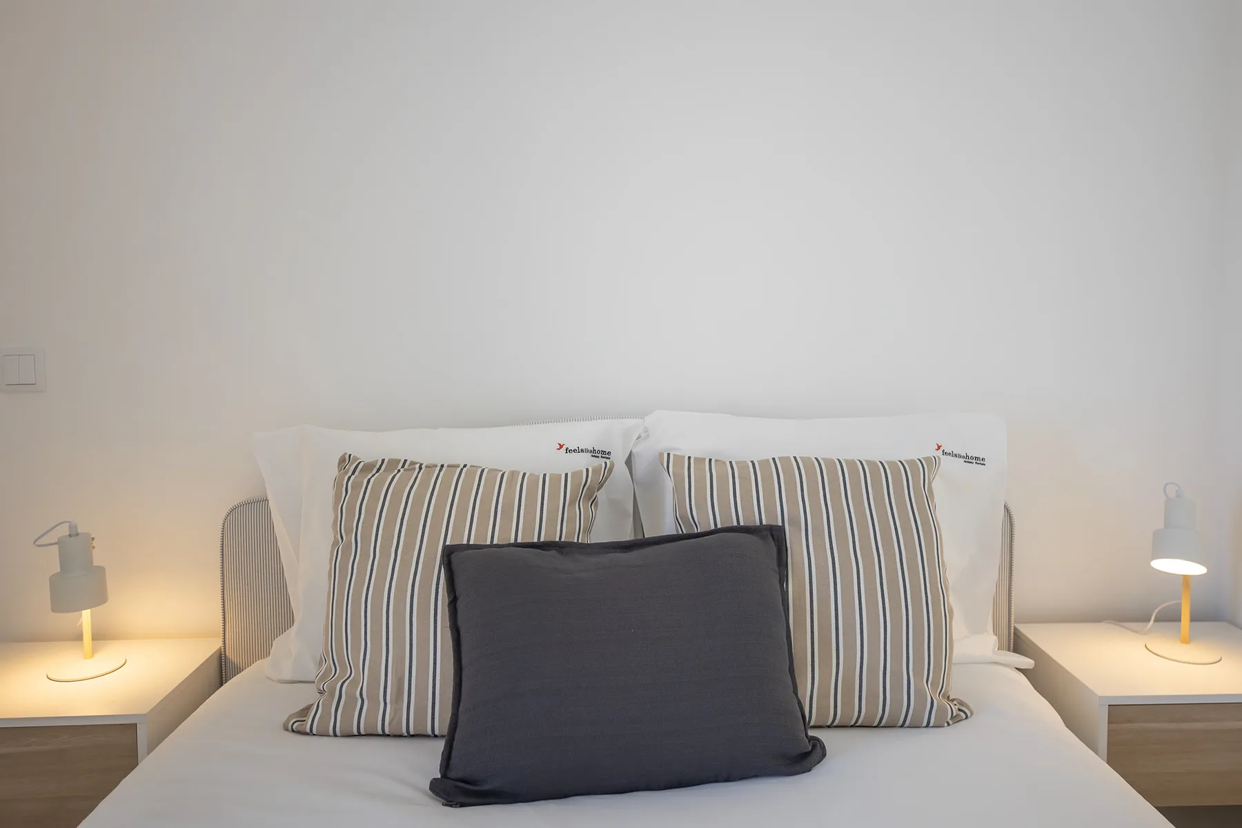 Un dormitorio con una cama, almohadas a rayas y lámparas de noche.