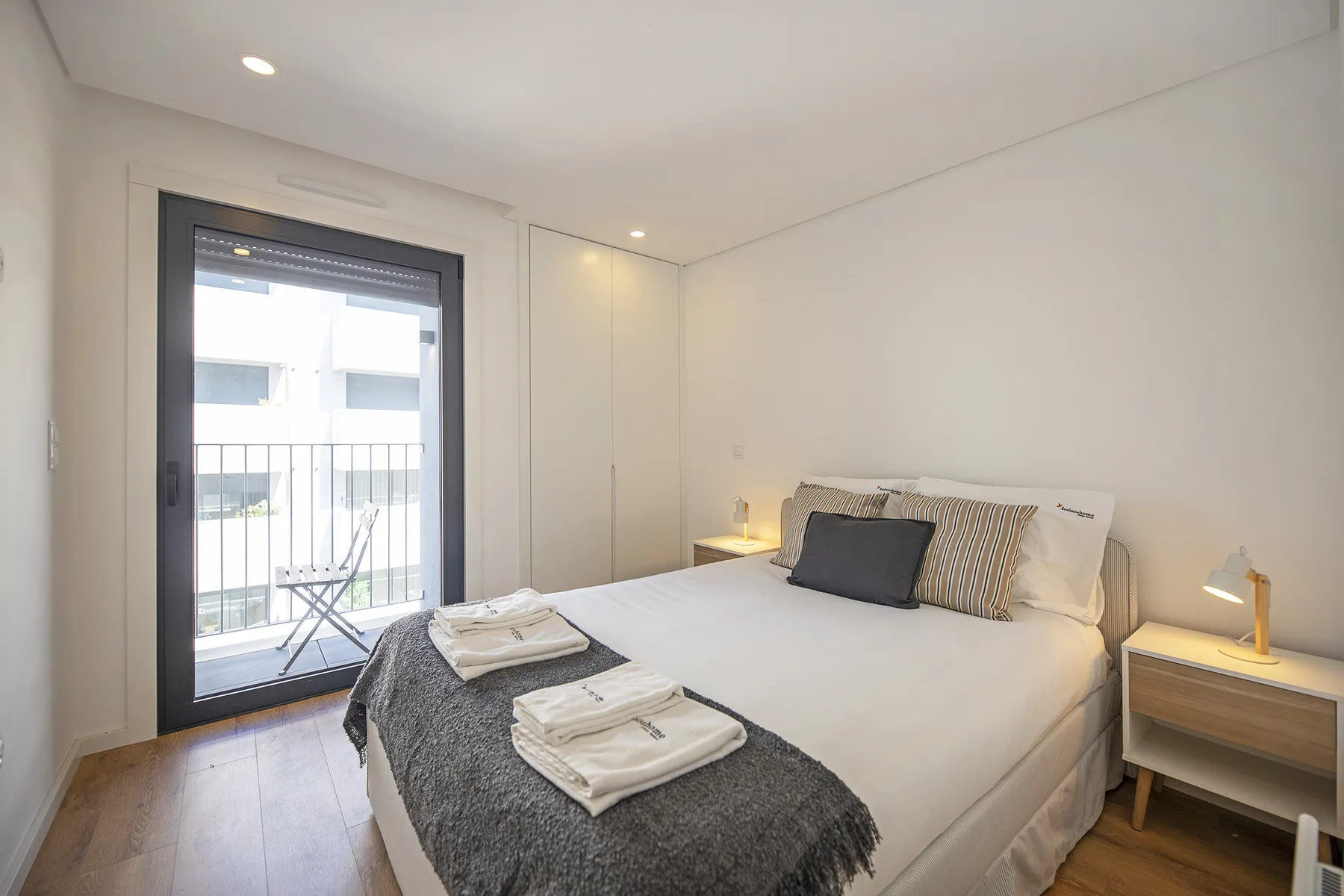 Un dormitorio luminoso con una cama doble y una puerta acristalada que da a un balcón.