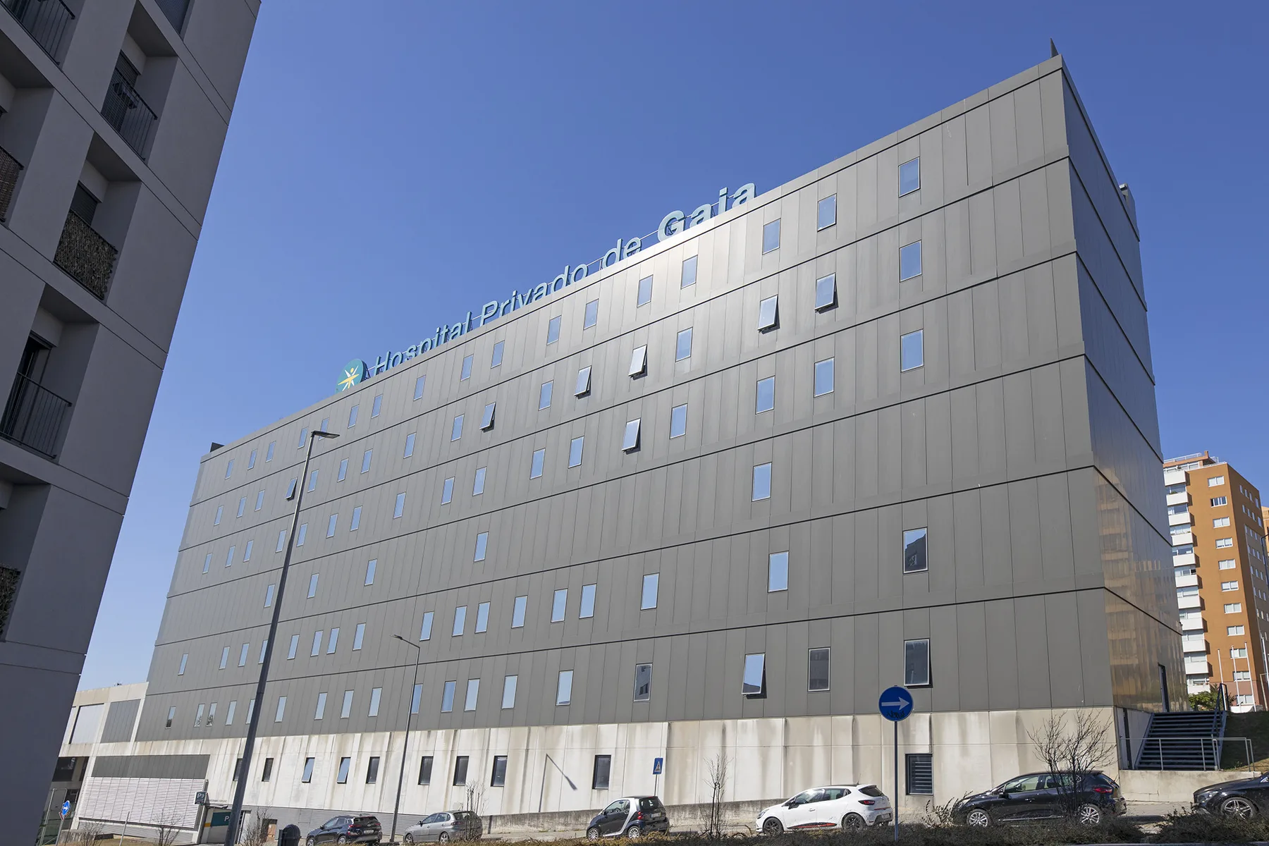 Un edificio moderno de varios pisos con filas de ventanas se alza bajo un cielo azul despejado.
