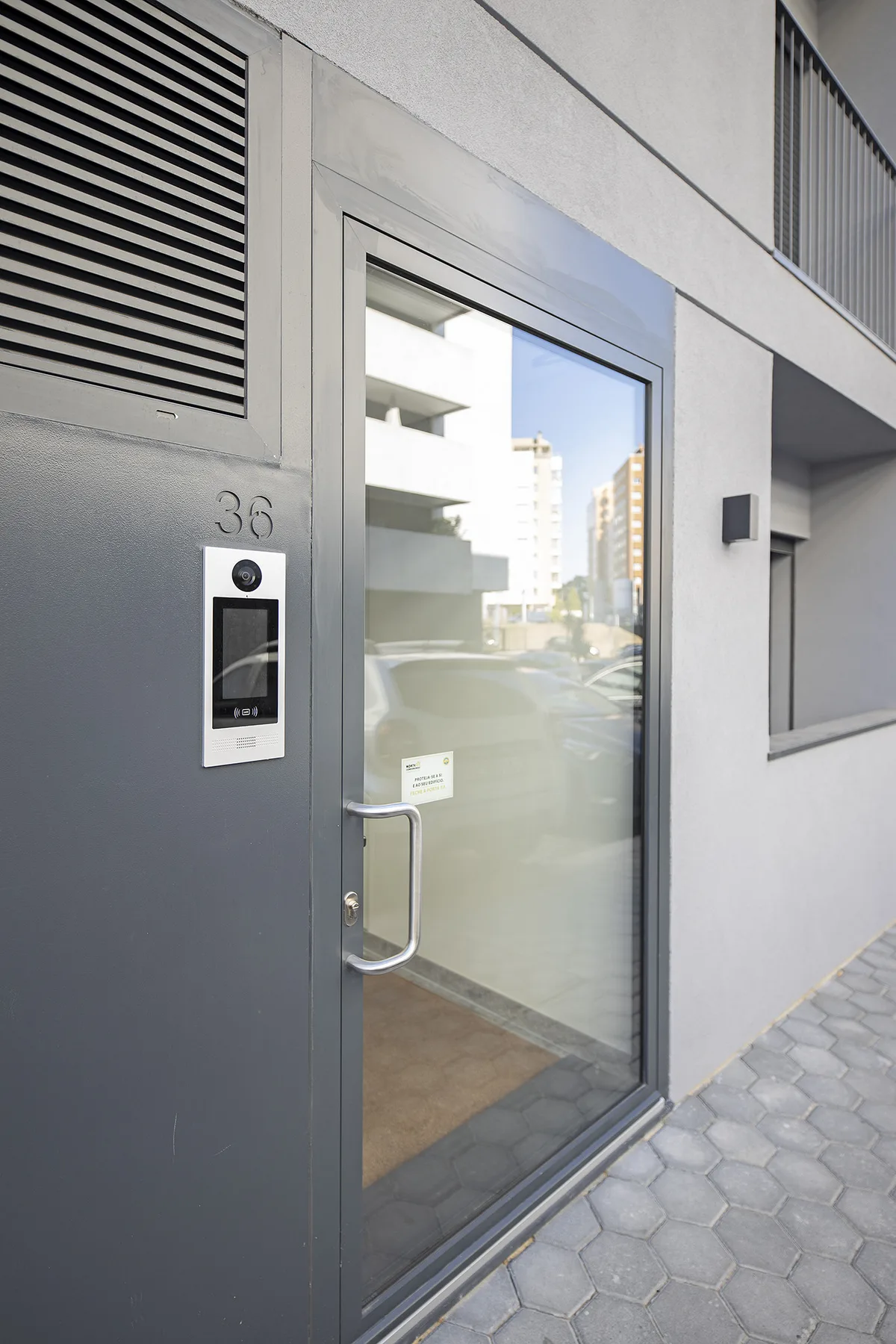Una puerta de entrada de vidrio junto a un interfono da a un camino pavimentado.