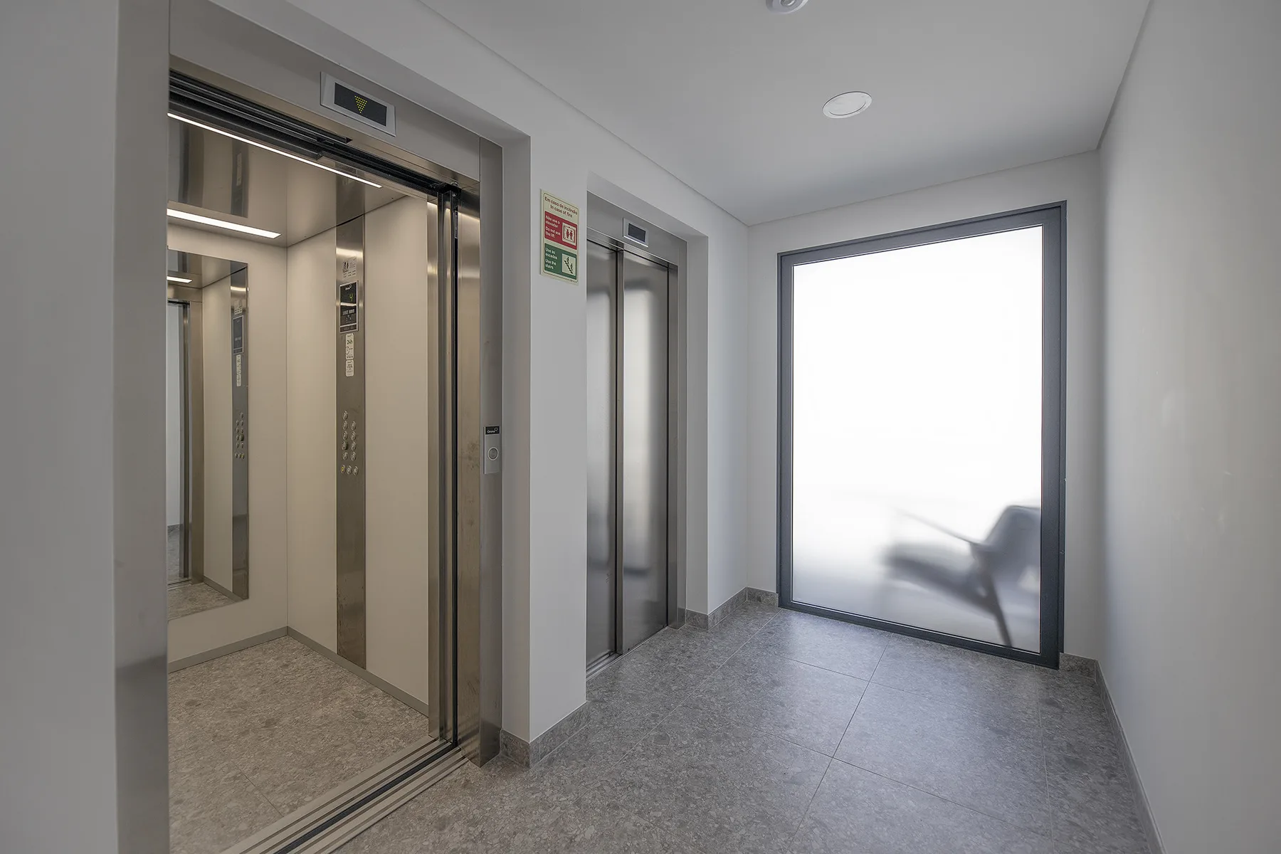 An elevator lobby with two elevators and a large bright window.